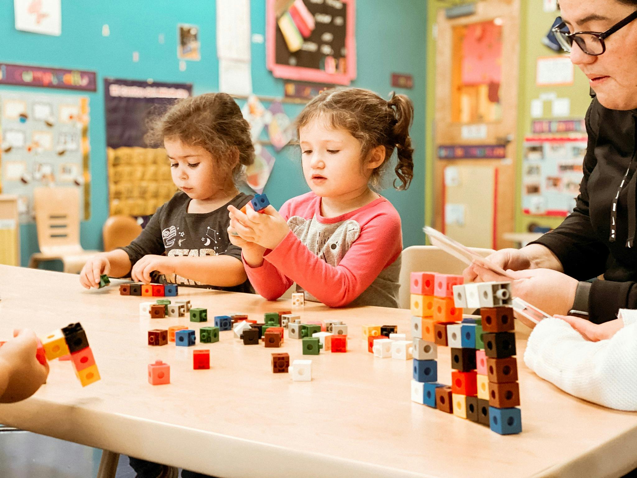 Two children and an adult playing with colorful interlocking blocks at a table