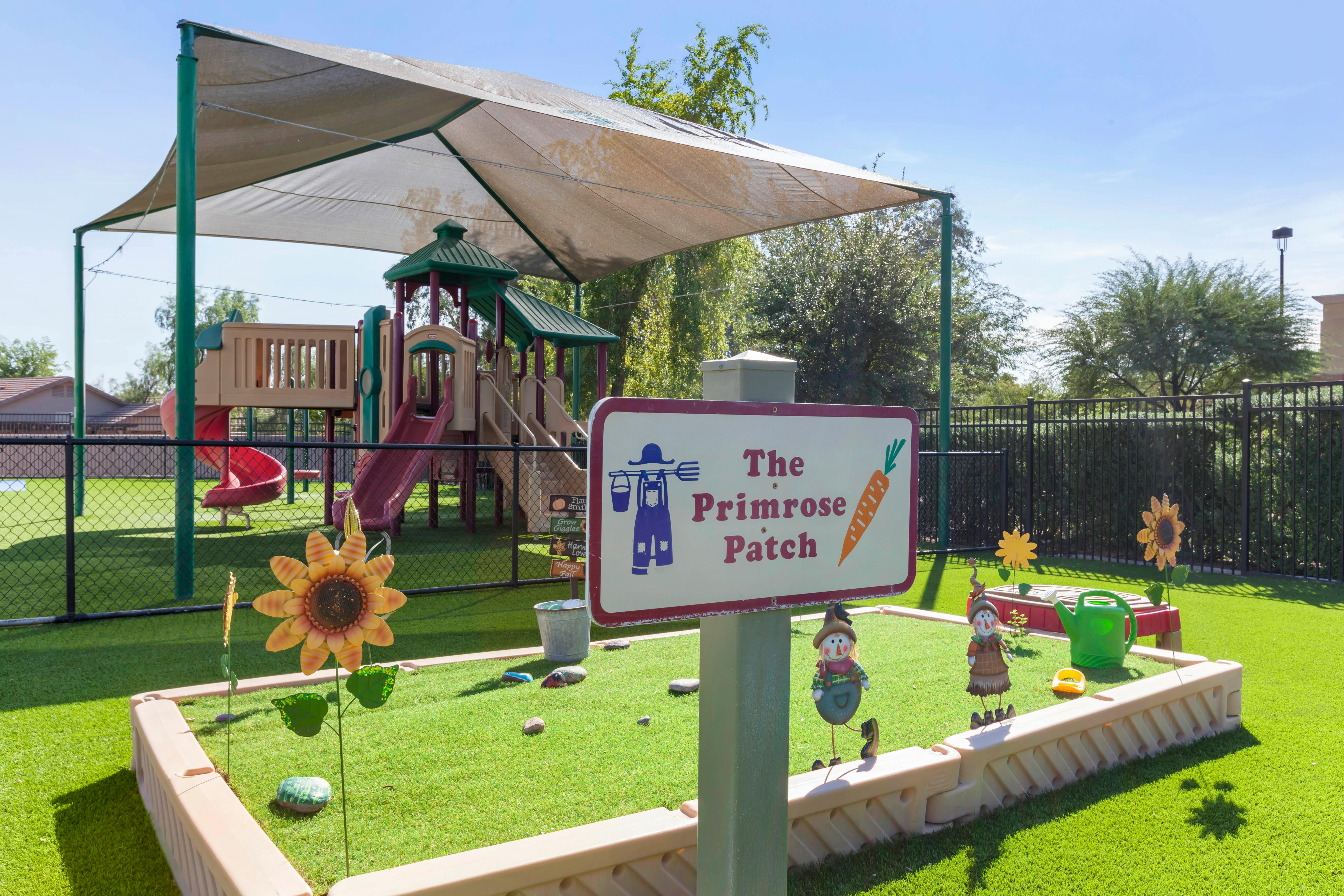 Sign for "The Primrose Patch" with playground equipment and shade sails in the background