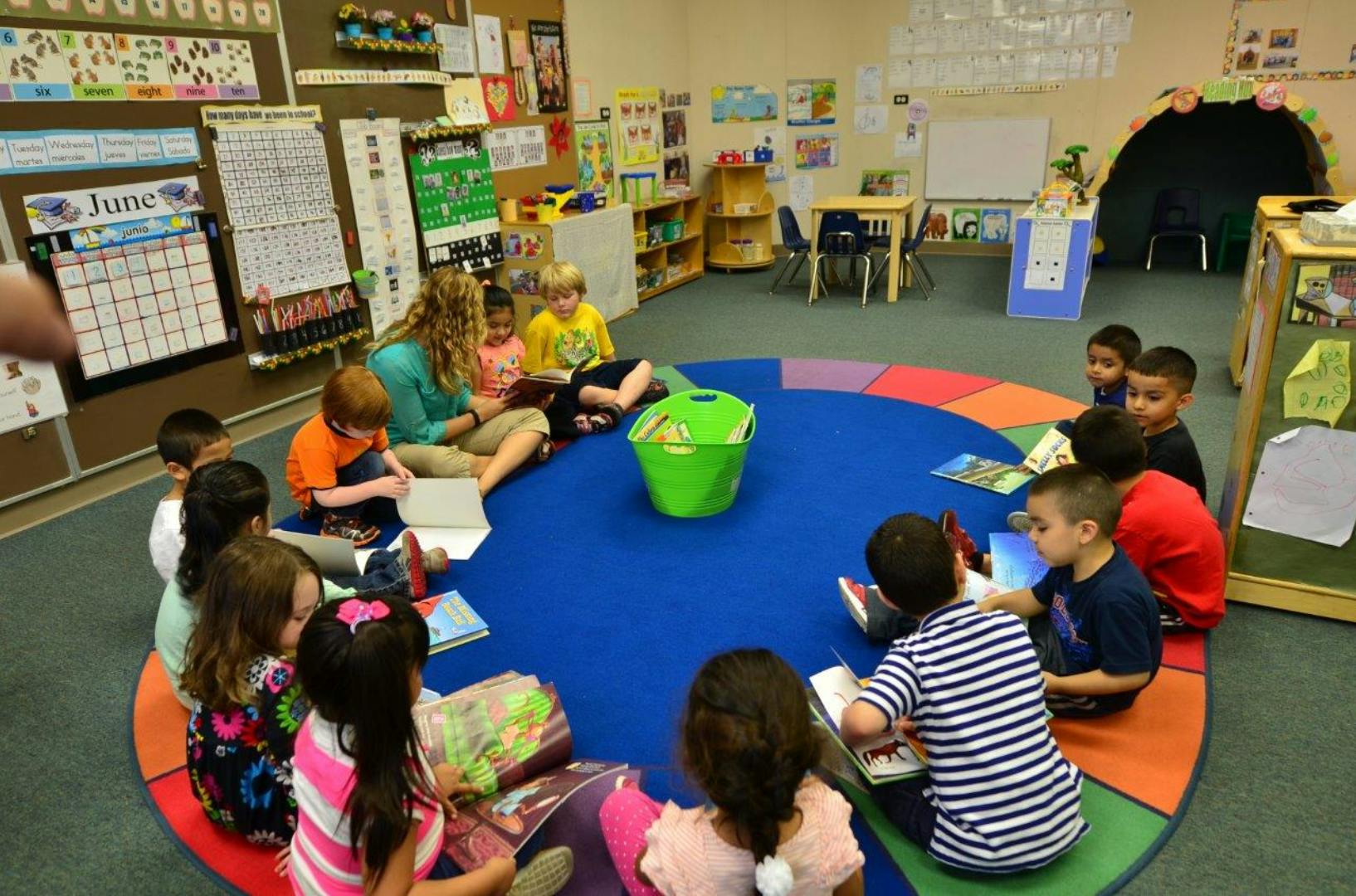 Adult and children sitting on a colorful rug in a classroom