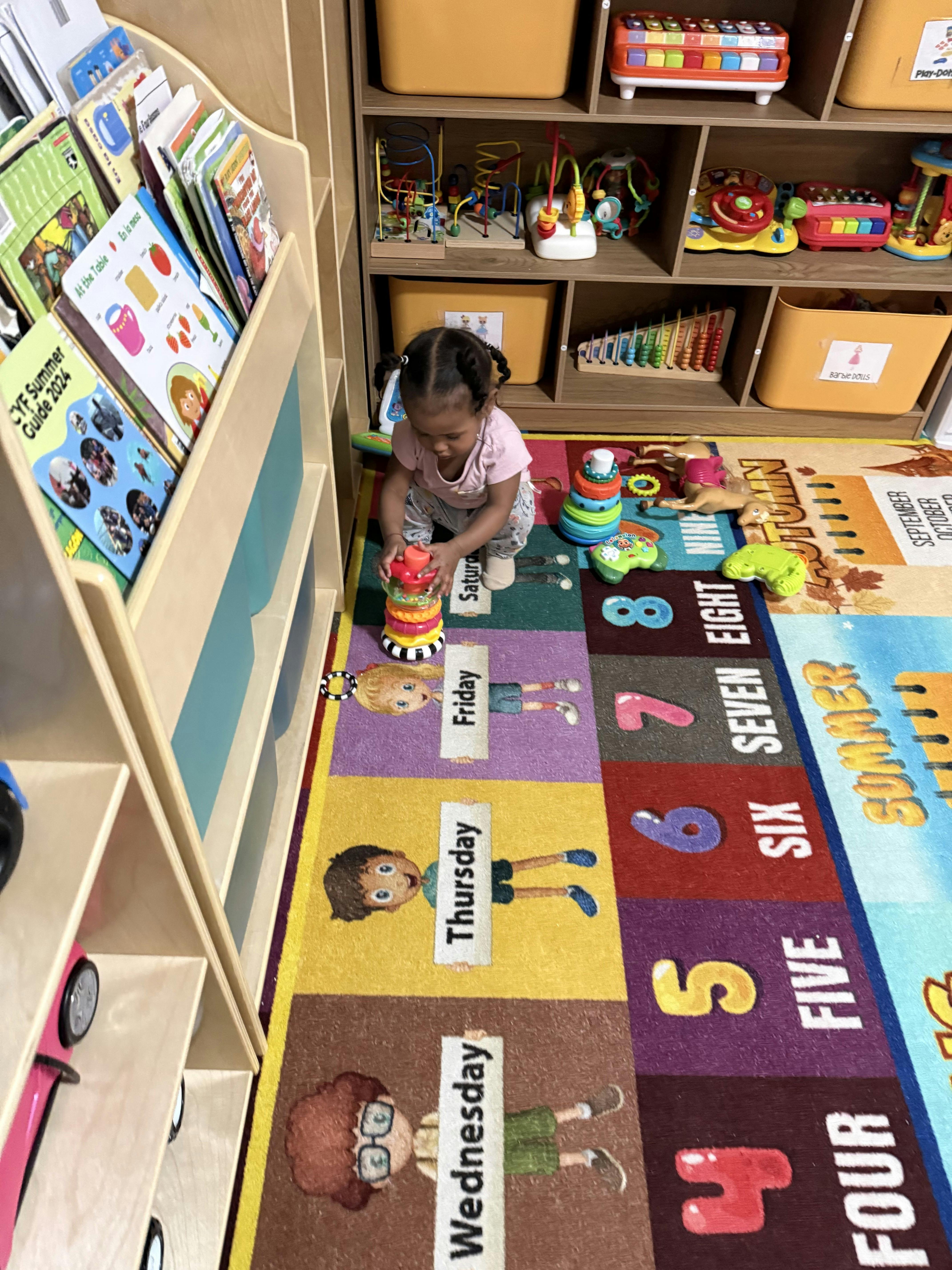 Child crouching on a colorful rug playing with stacking rings