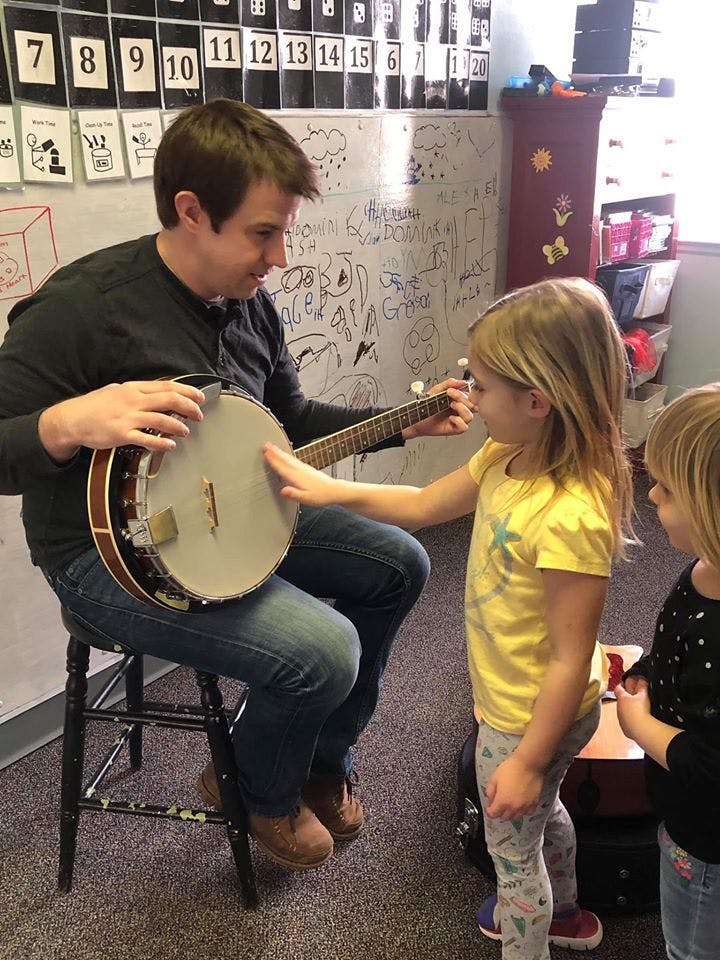 Person playing banjo for two children