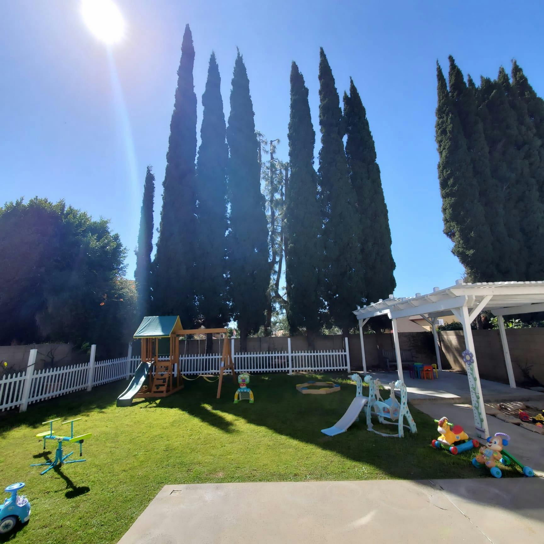 Backyard playground with swings, slides, and a white picket fence