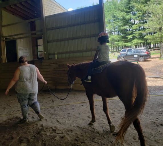 Child riding a horse led by a person