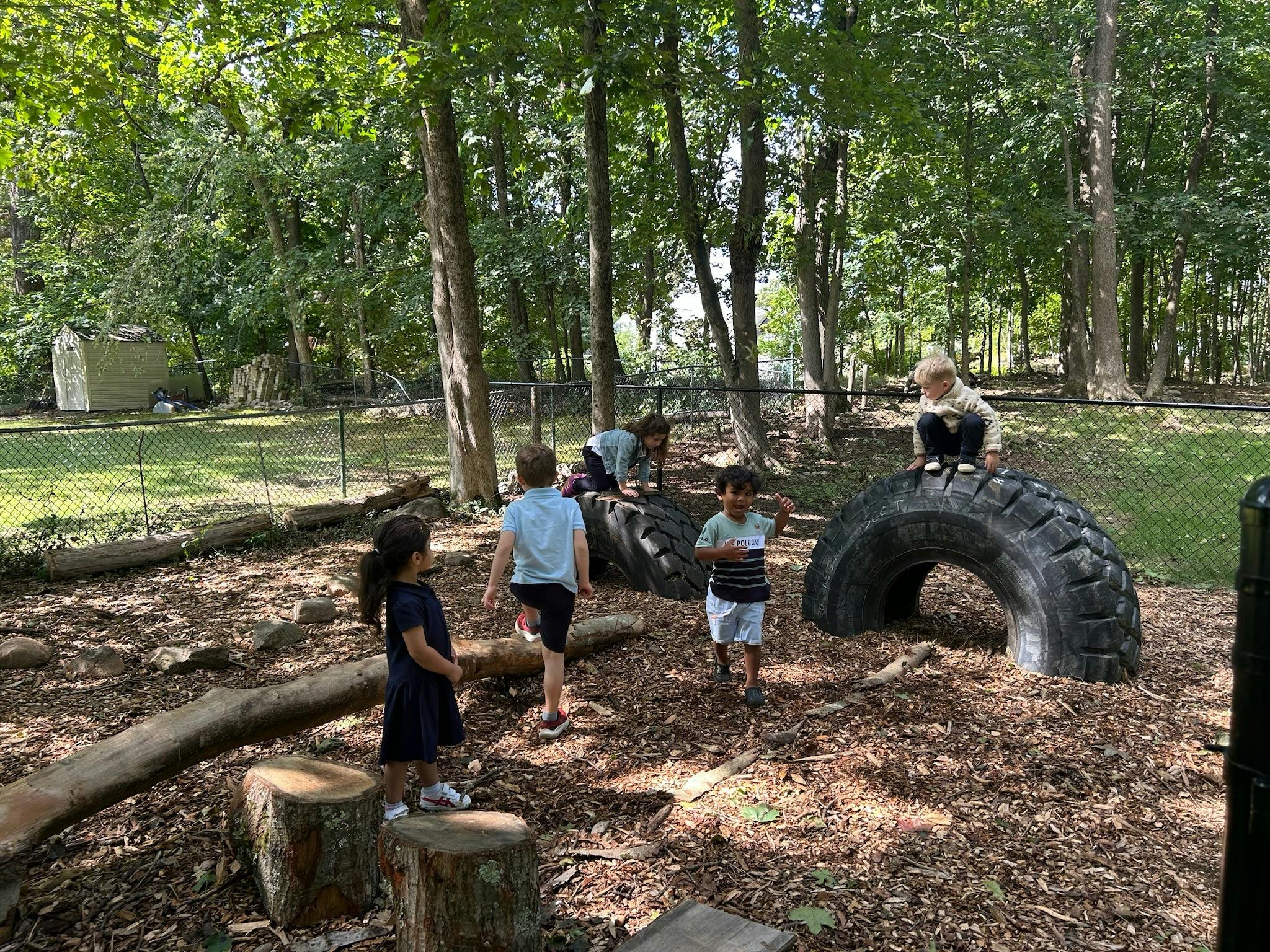 Children playing with large tires and tree logs outdoors