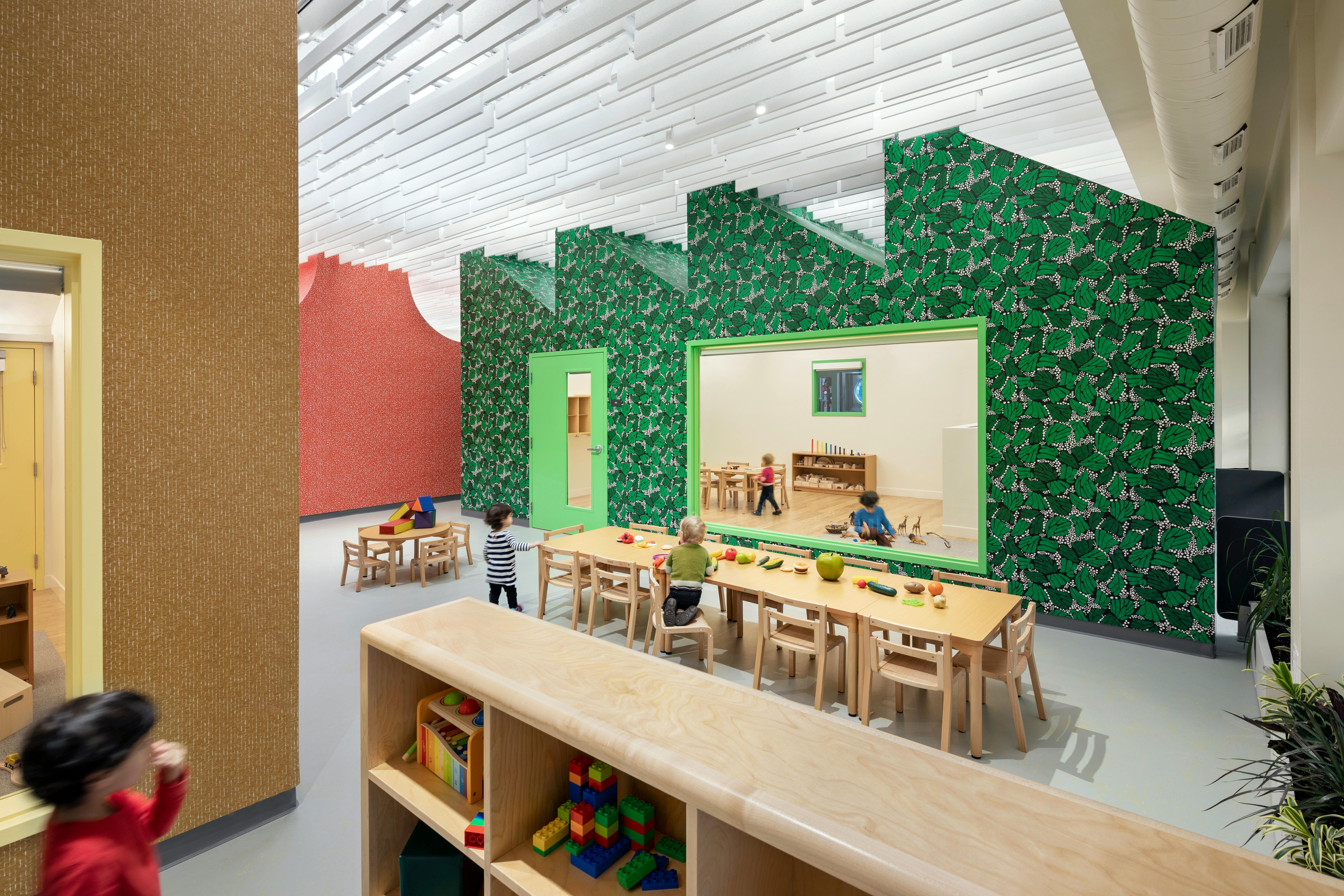Children and adults in a classroom with green leaf-patterned walls