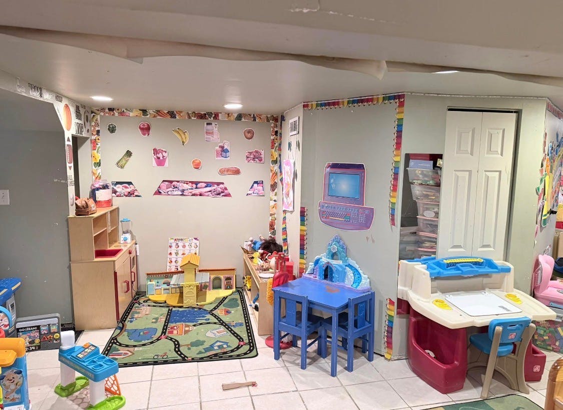 A playroom with various toys, including a play kitchen, a rug with roads, and a blue table with chairs