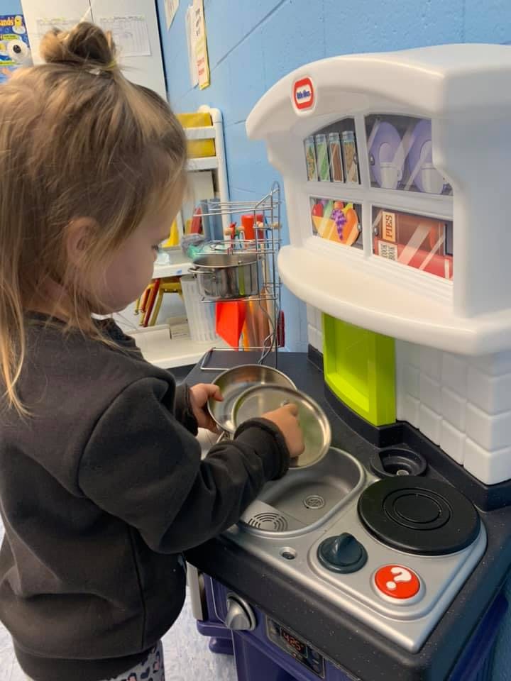 Child playing with a toy kitchen set, holding metal pots