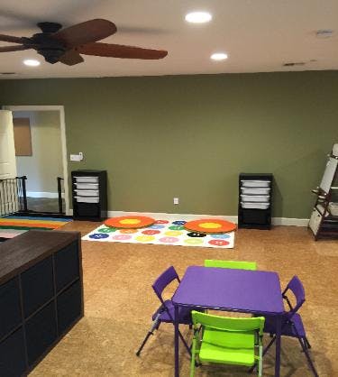 Playroom with small purple table and green chairs, colorful rug, and ceiling fan
