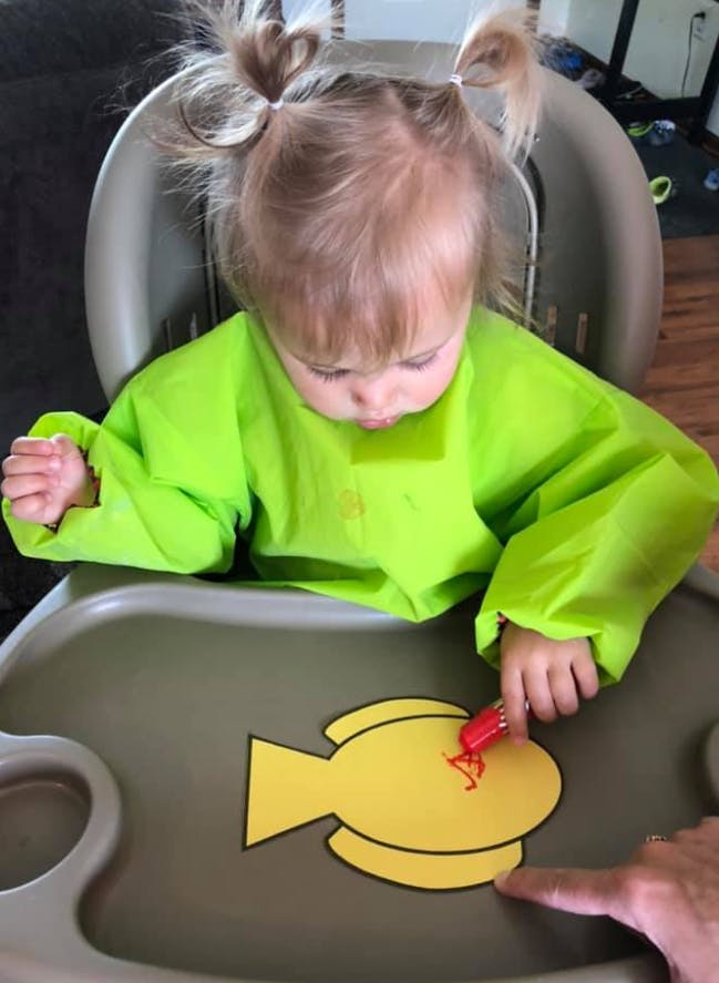 Child in high chair painting a yellow fish cutout