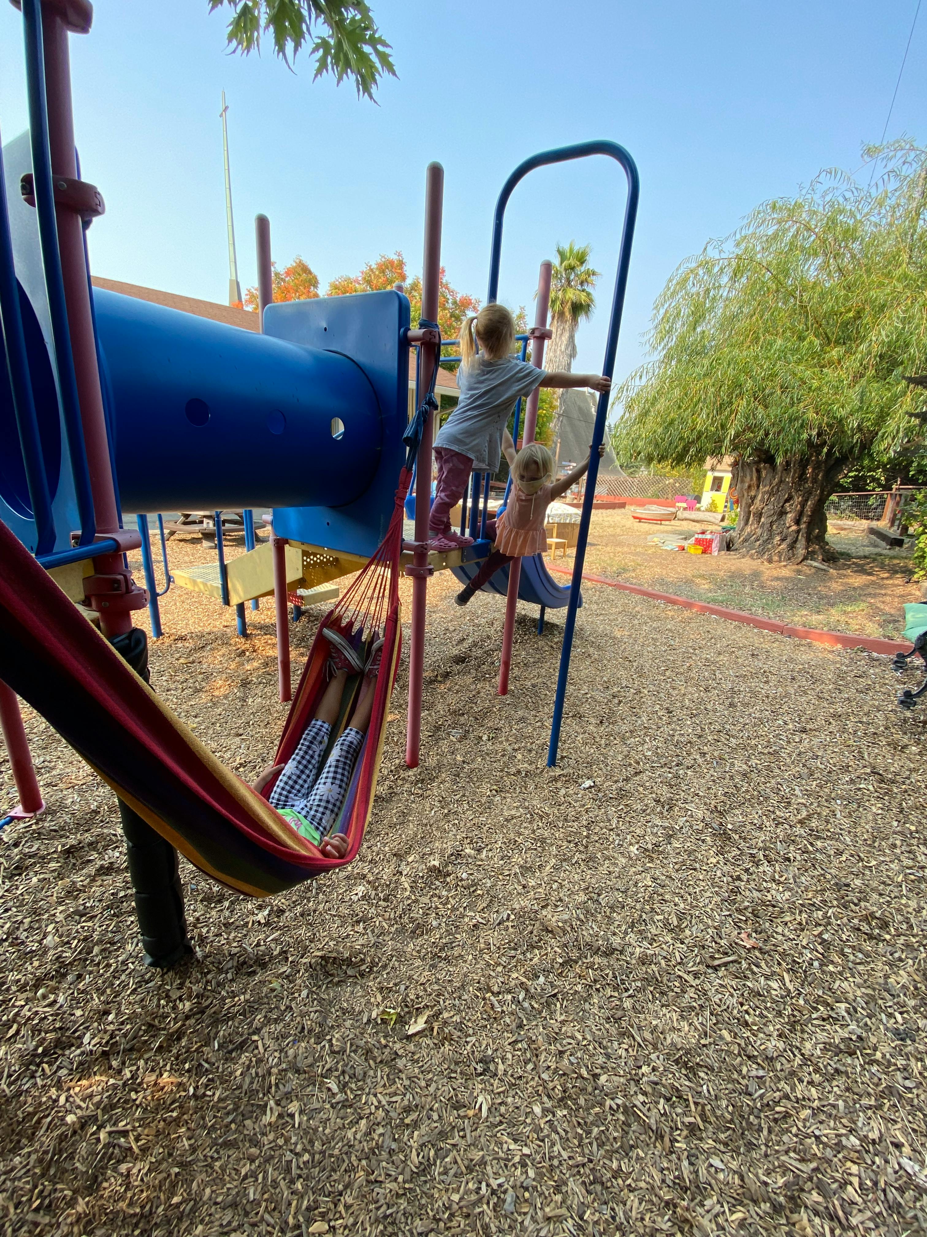 Two children on a playground climbing structure, one child in a hammock