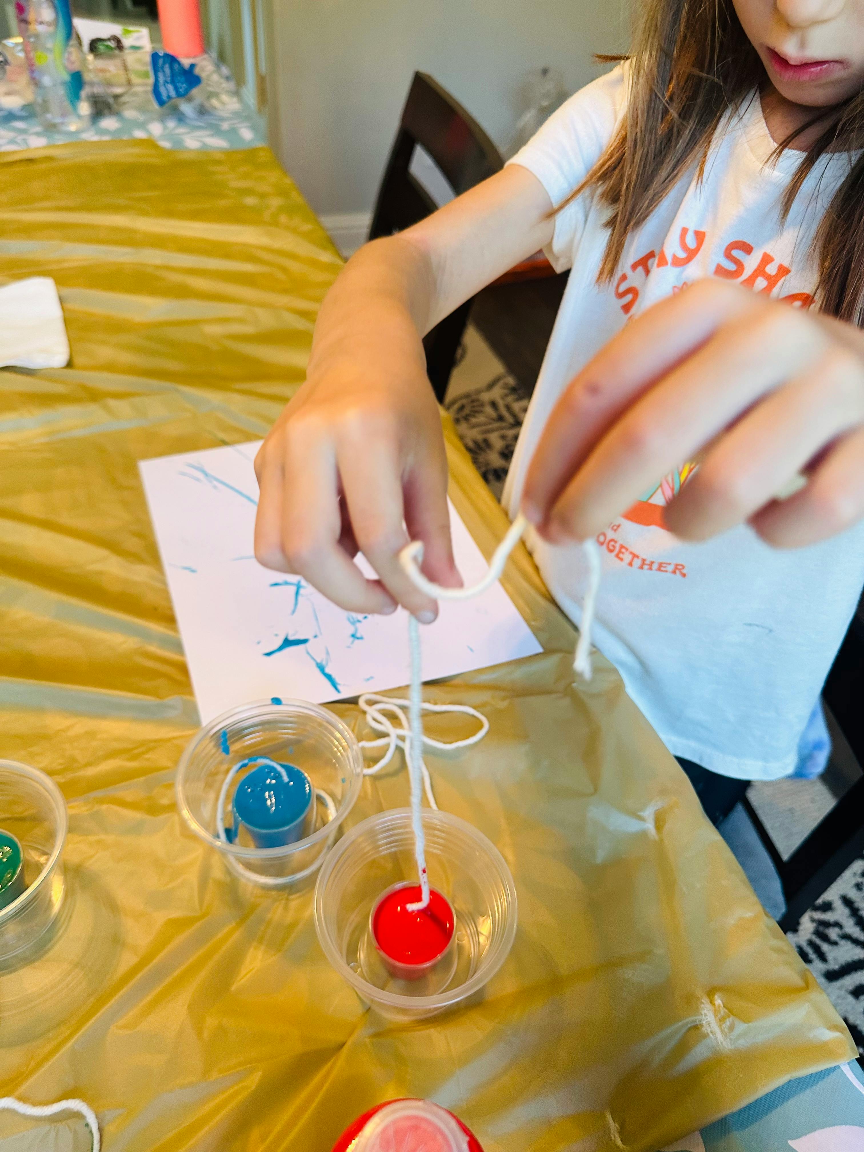 Child's hands holding string over paint cups
