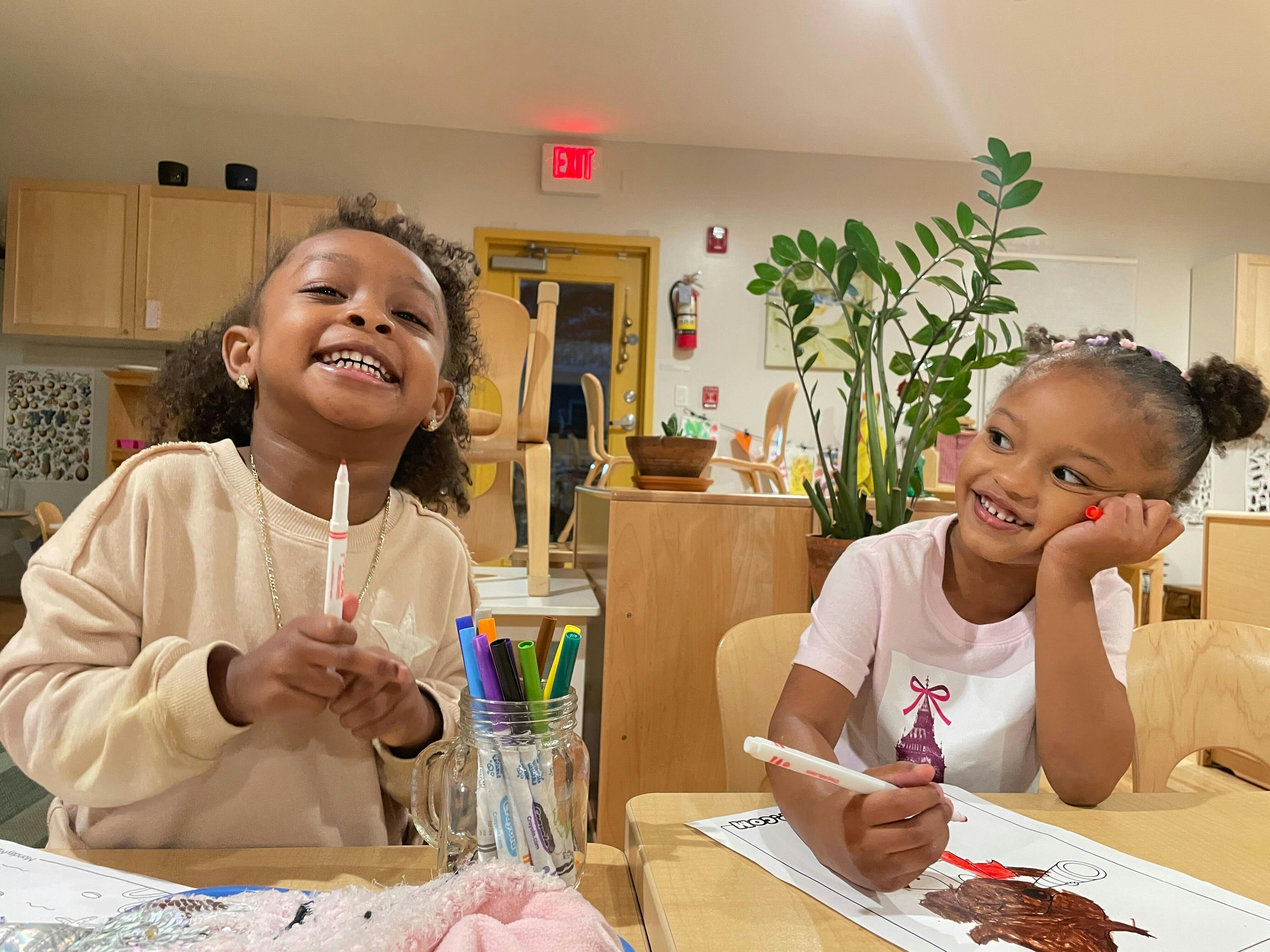 Two children sitting at a table with markers in a classroom