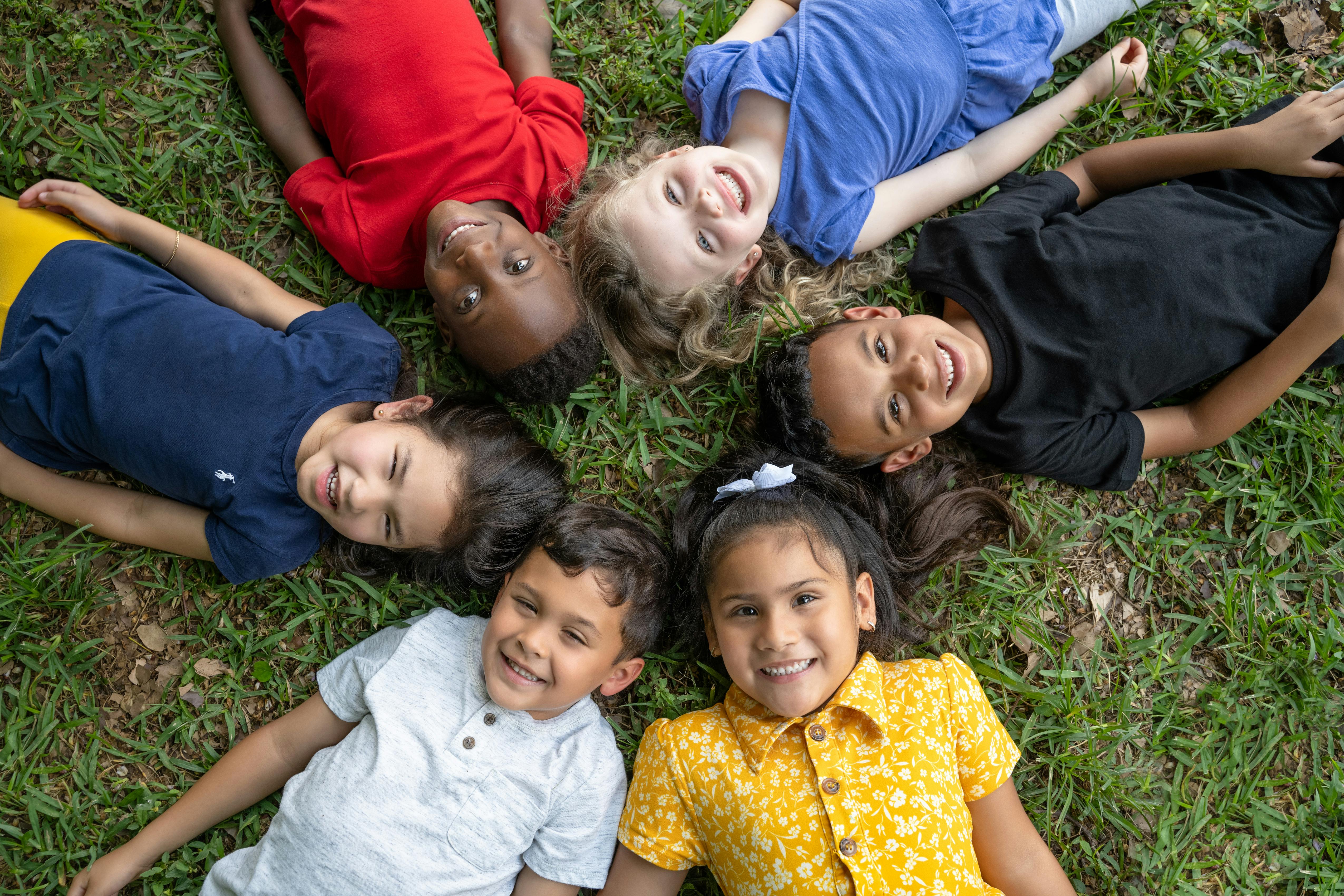 Six children lying in a circle on grass, looking up