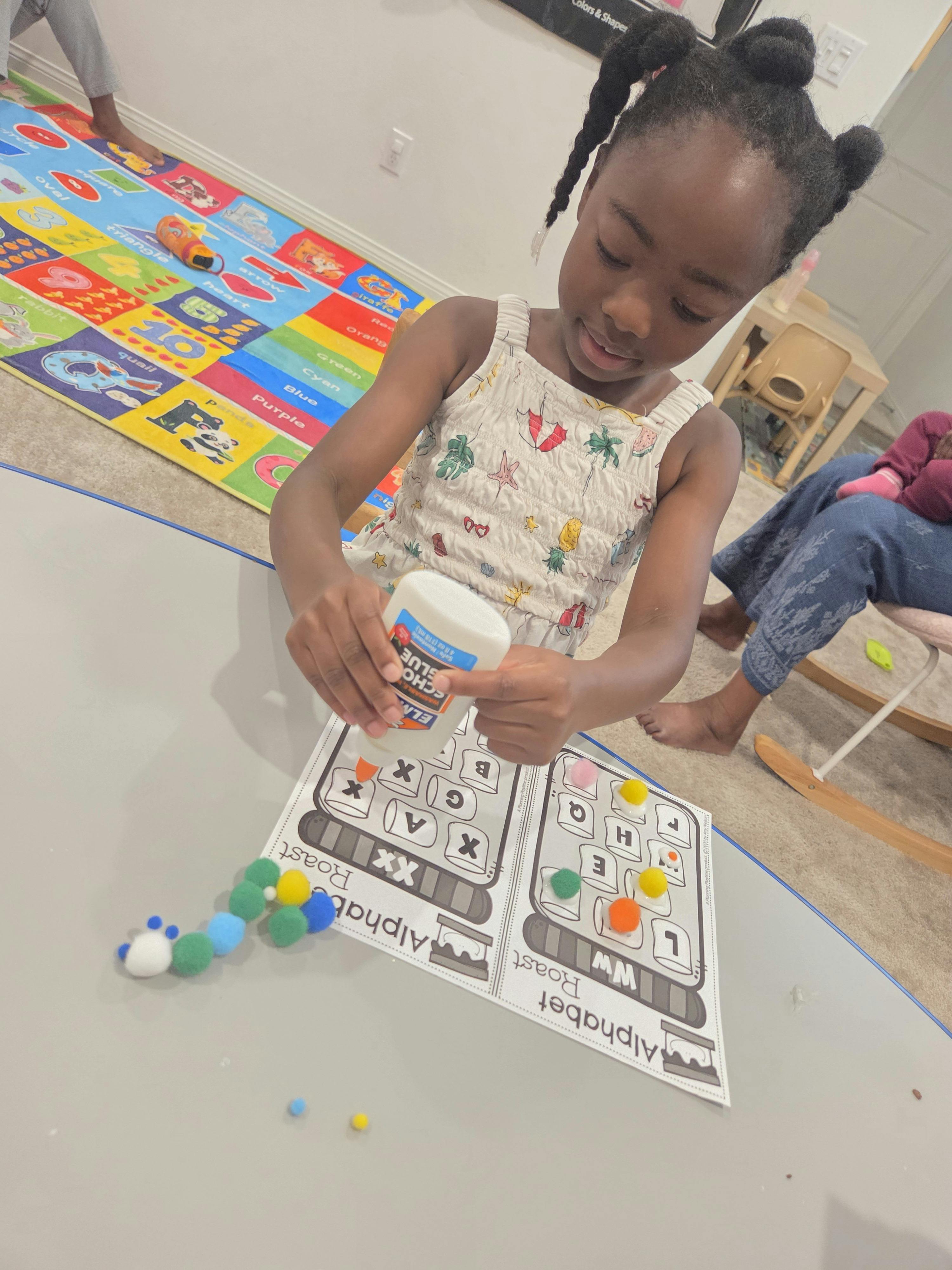 Child gluing pom-poms onto an alphabet worksheet at a table