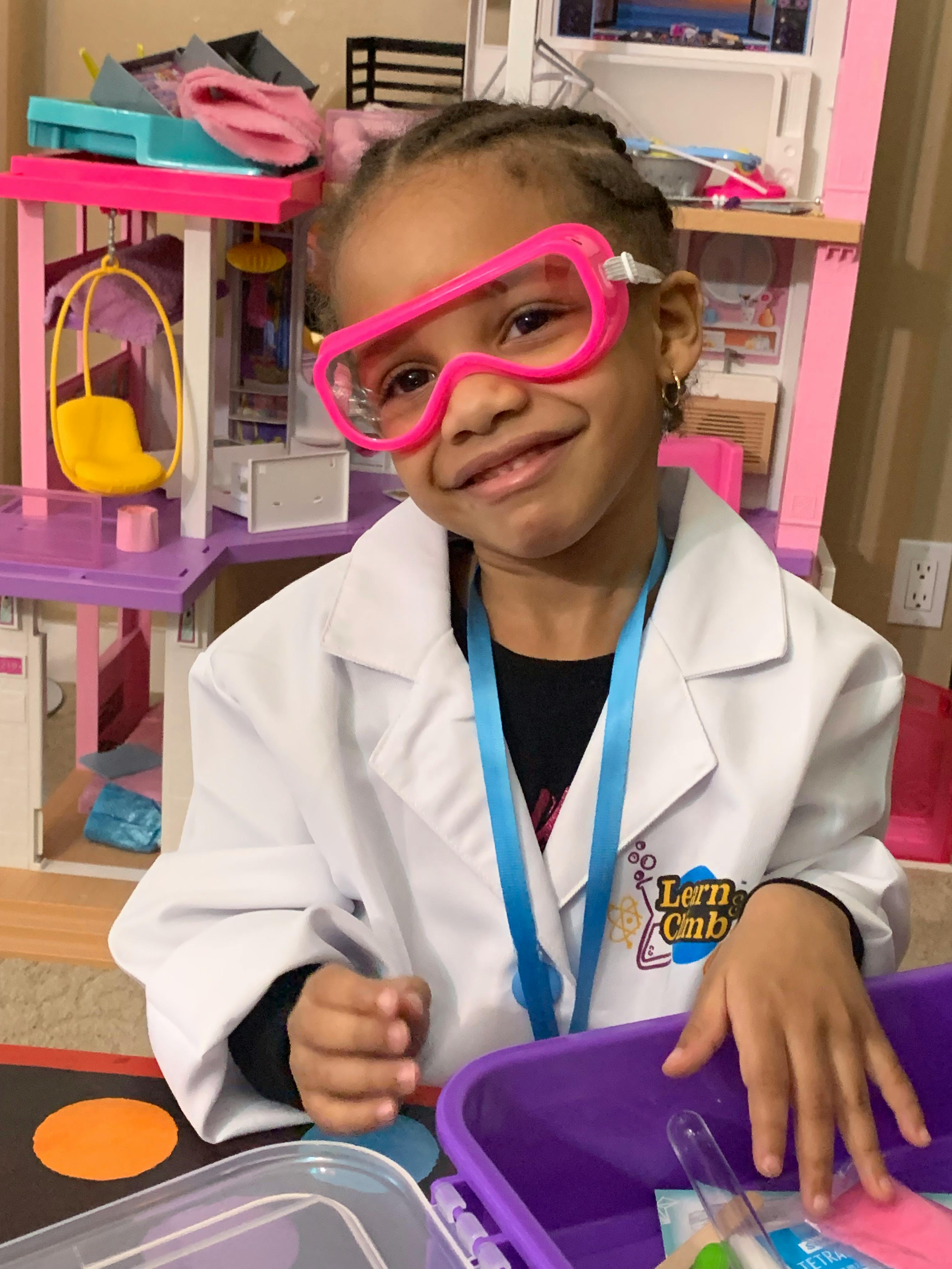 Child in a lab coat and pink safety goggles