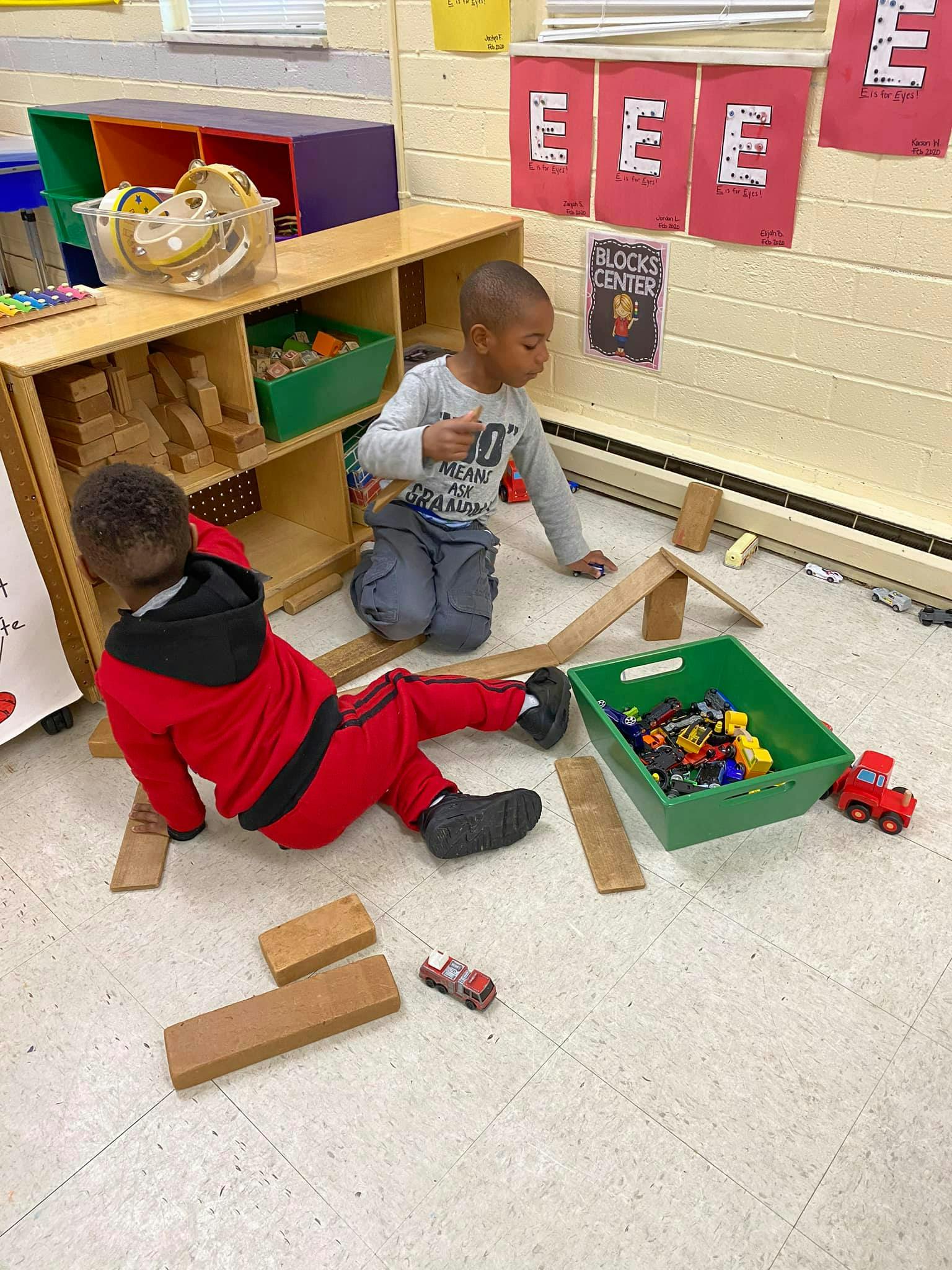 Two children playing with wooden blocks and toy cars on the floor
