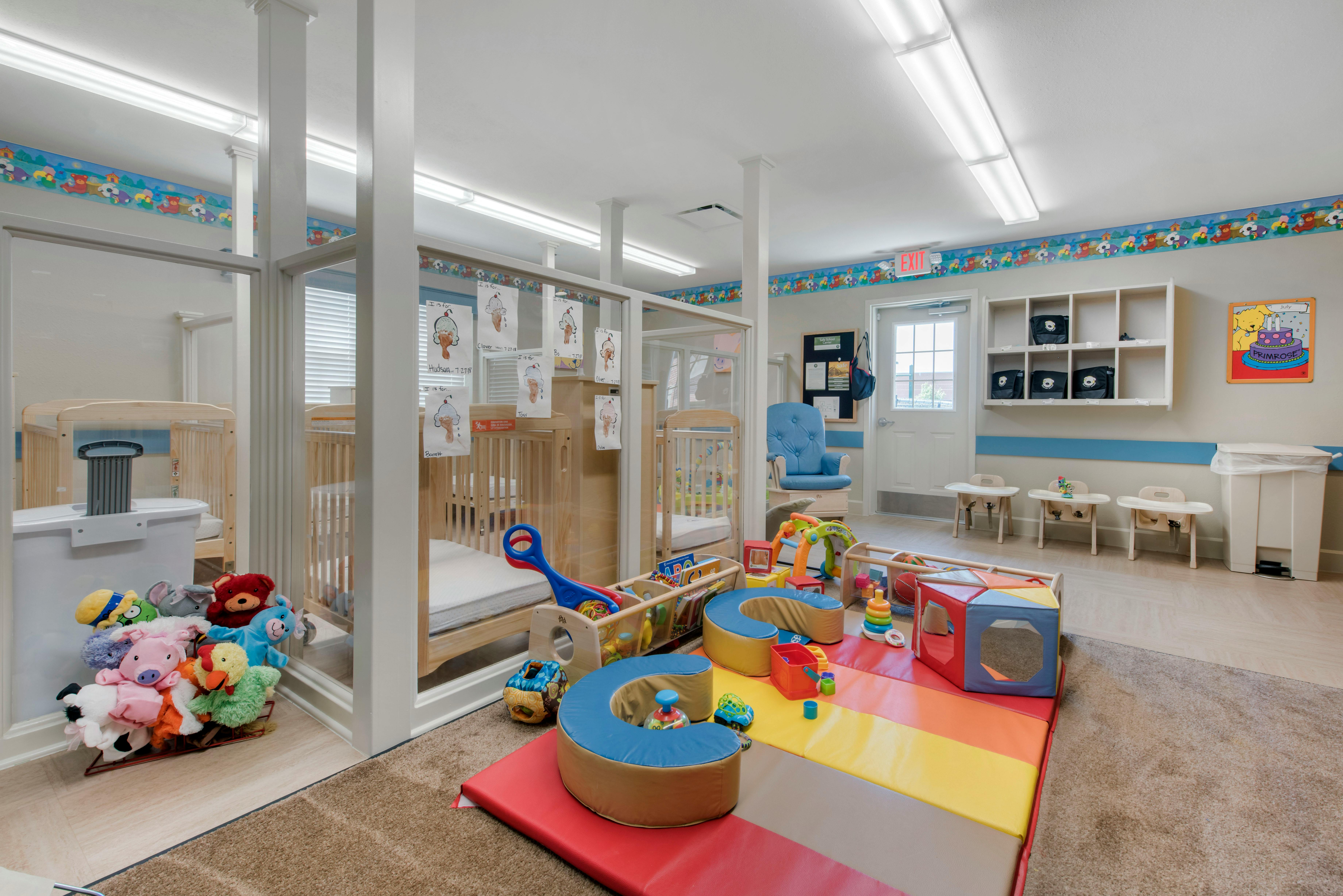 A childcare classroom with cribs, playmats, toys, and small high chairs