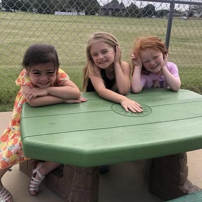 Three children sitting at a green picnic table outdoors