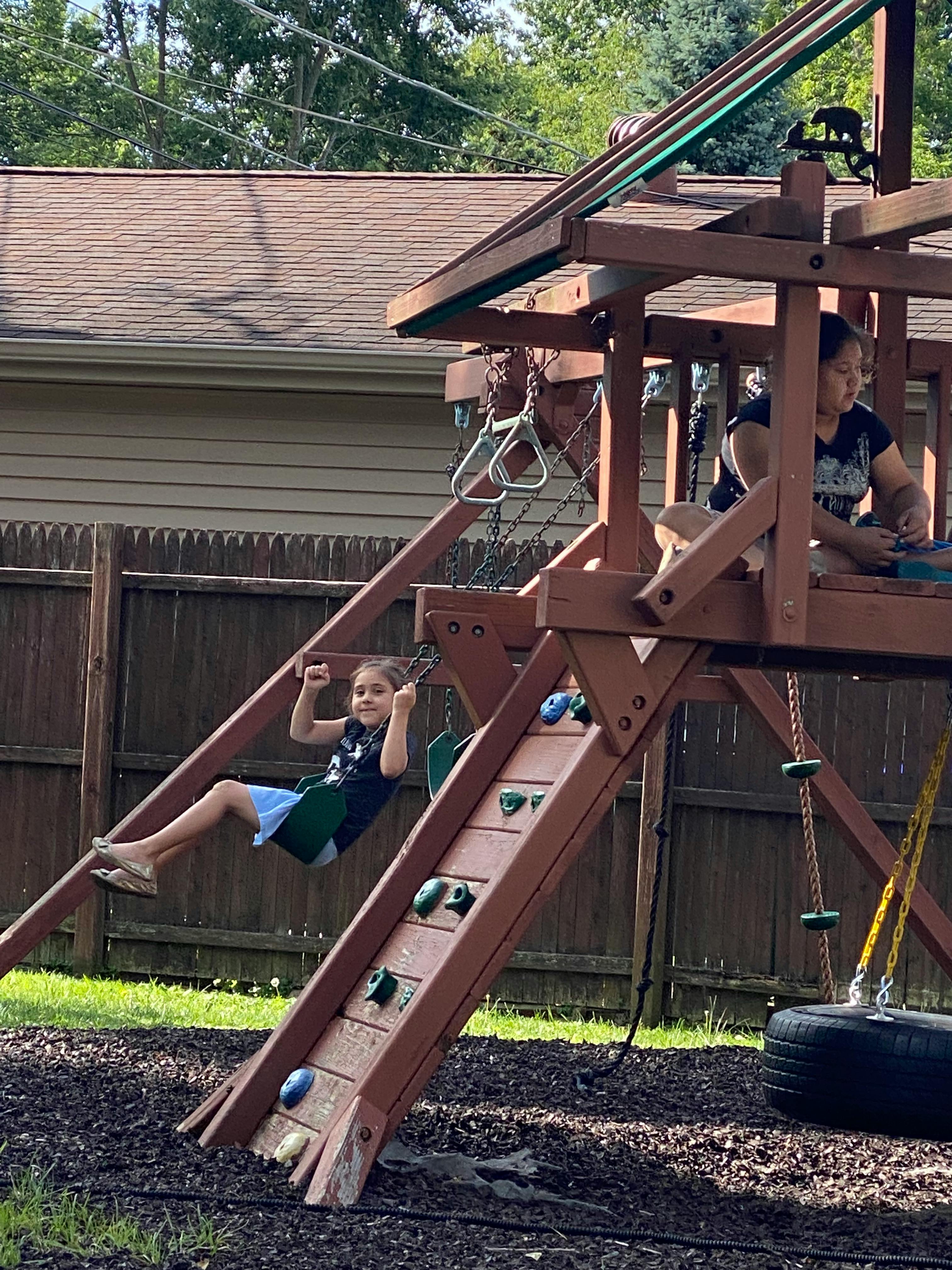 Child on a swing set, another child on the play structure