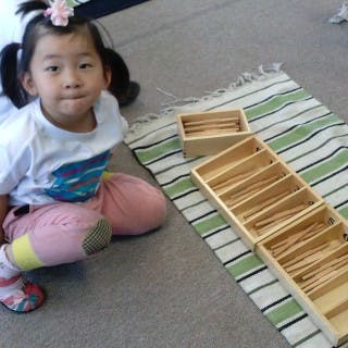 Child sitting on floor next to wooden Montessori materials