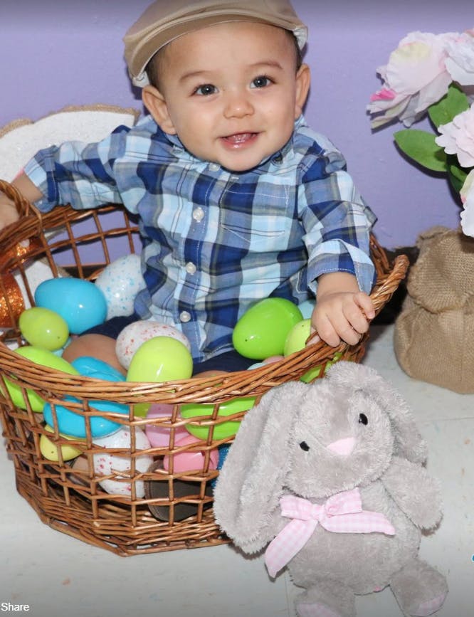 Child in a plaid shirt and cap sitting in a basket with plastic eggs