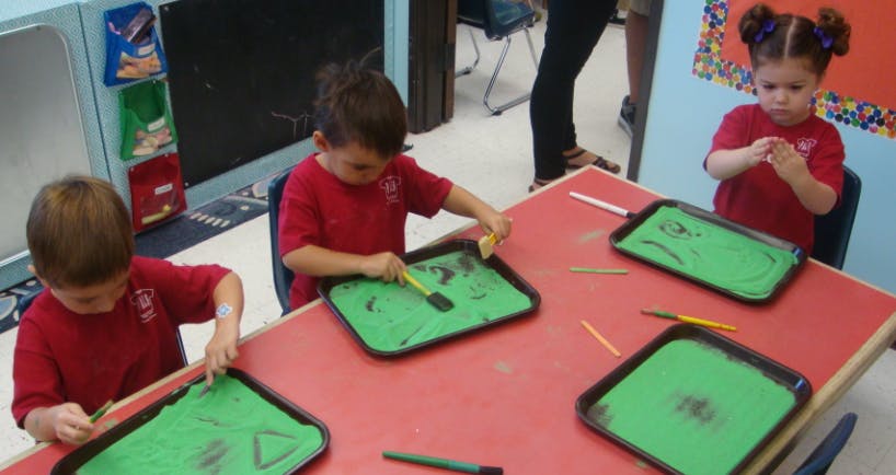 Children drawing in green sand trays at a table