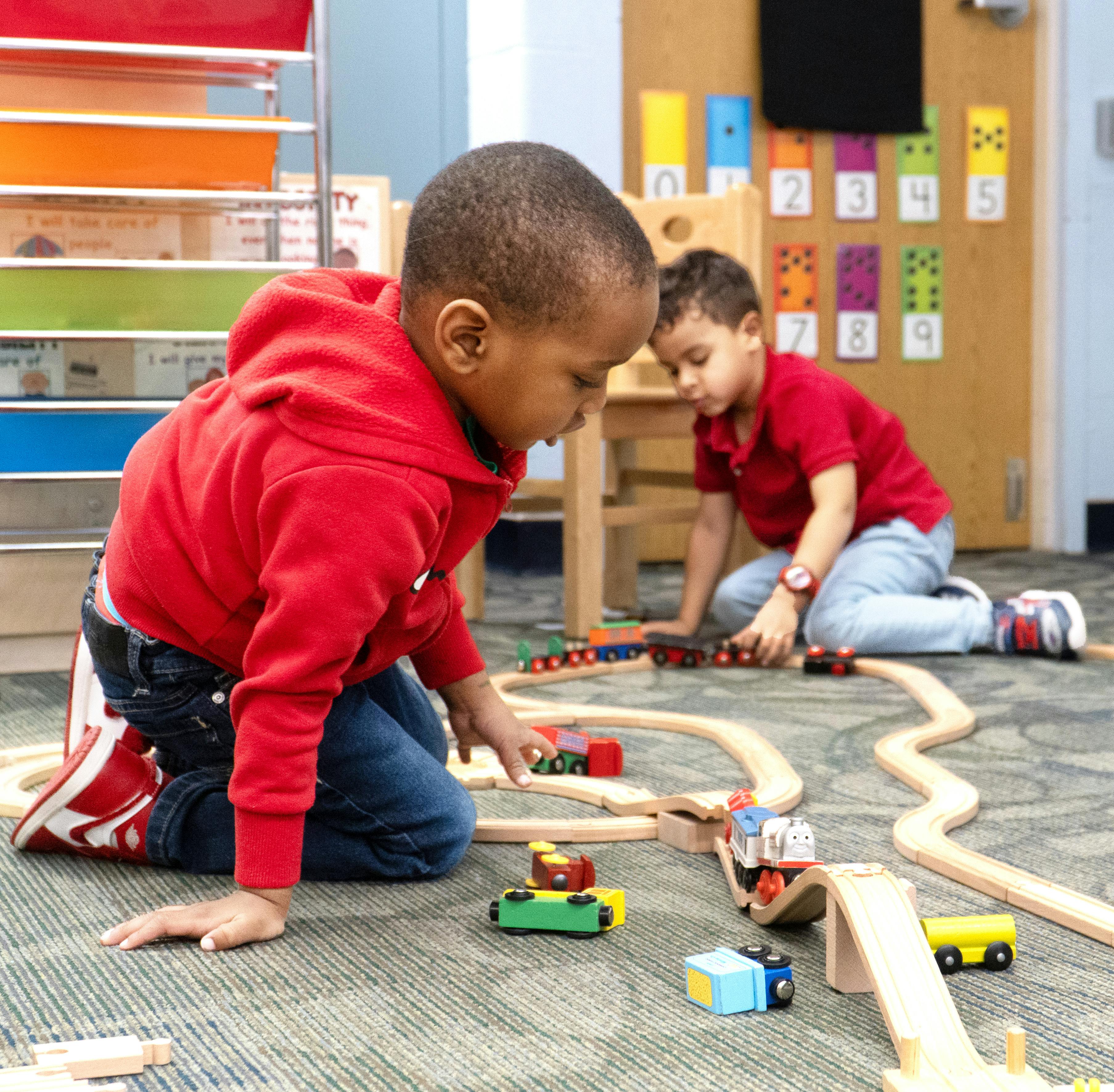 Two children playing with a wooden train set on the floor