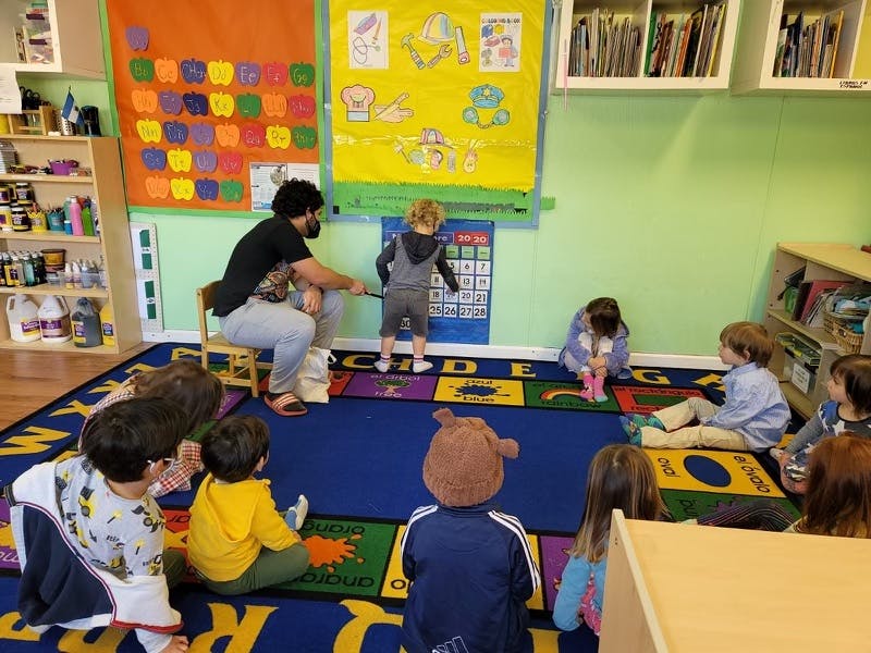 Adult and children in a classroom, one child points to a chart