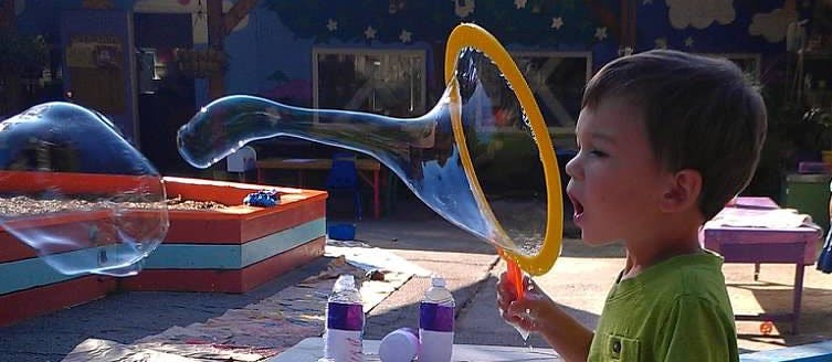 Child blowing a large bubble with a bubble wand