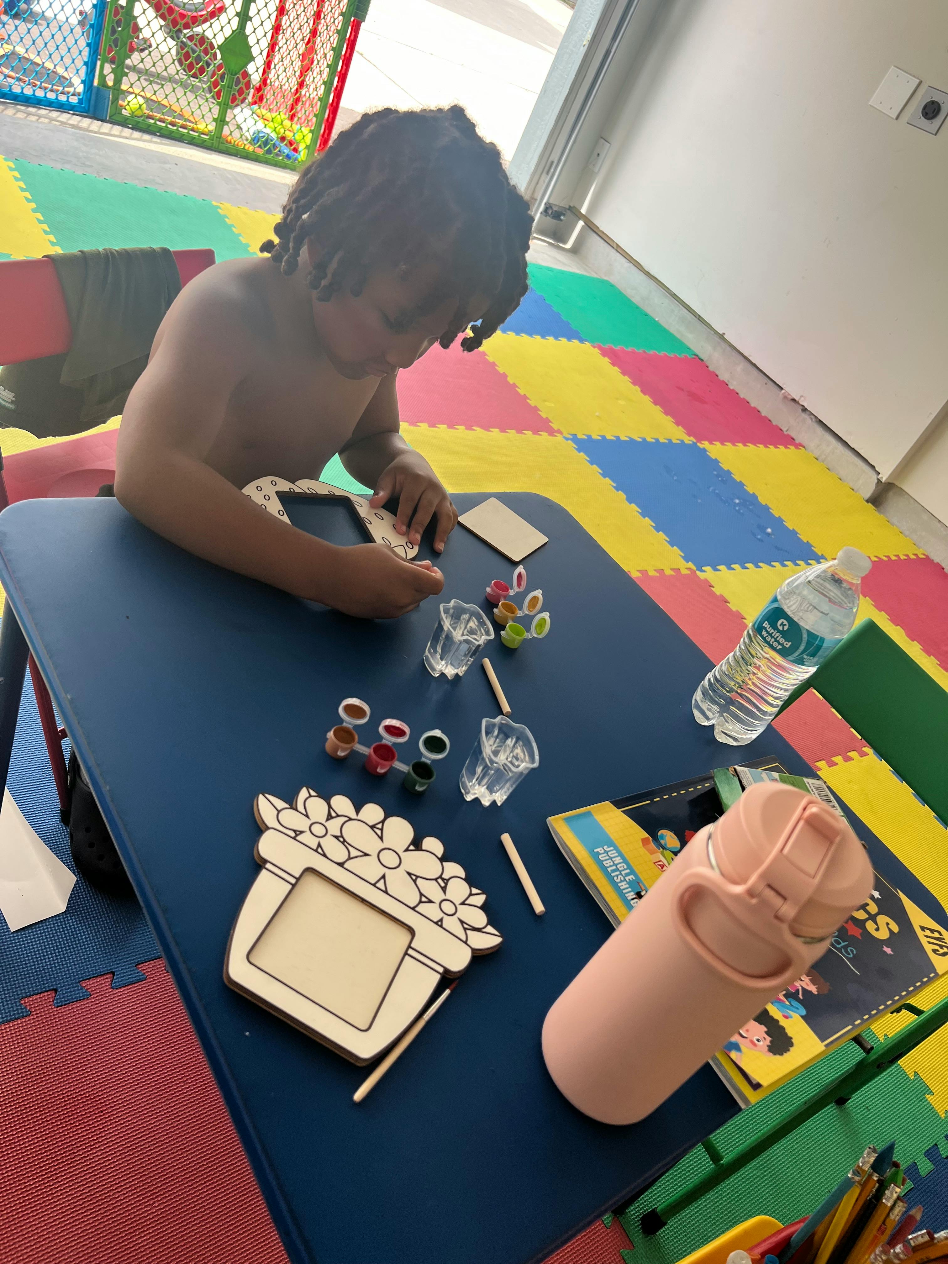 Child painting a wooden frame at a table