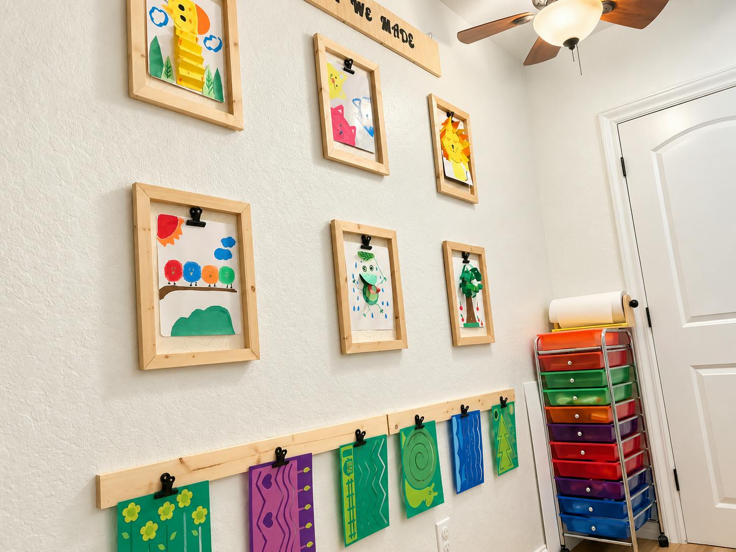 Child artwork displayed in wooden frames and on a wall-mounted rail