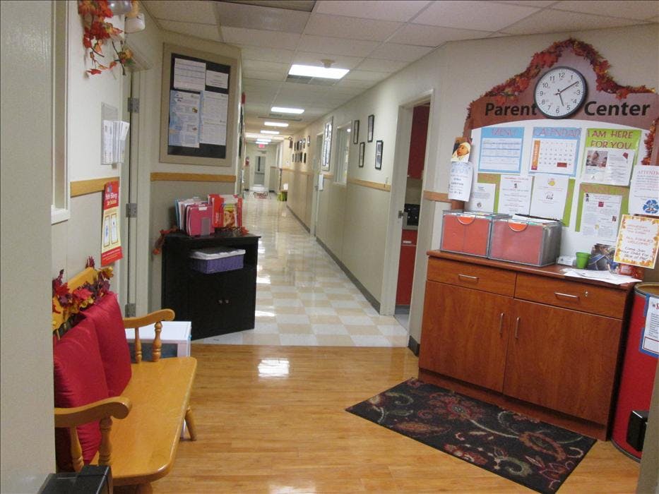 A long hallway with multiple doors and bulletin boards, and a wooden bench with red cushions