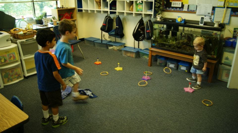 Three children playing with rings on the floor in a classroom