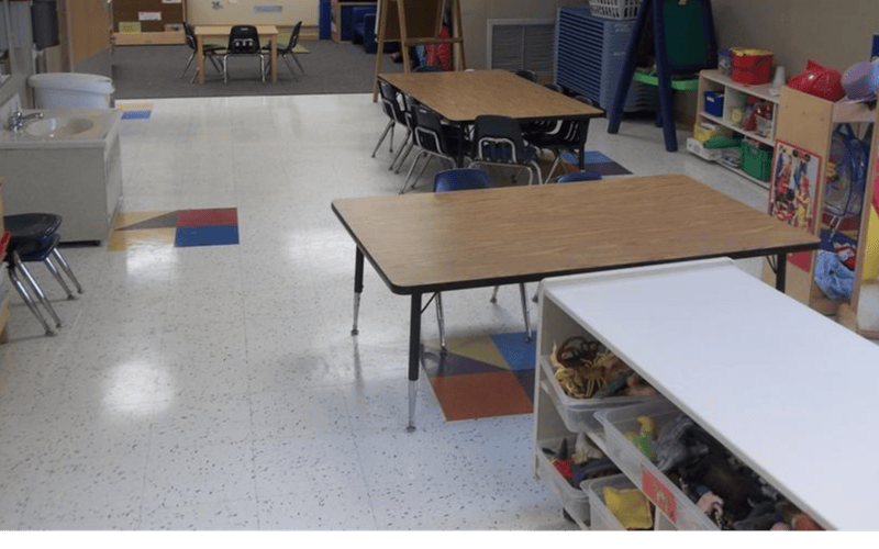 Classroom with child-sized tables and chairs, a sink, and storage shelves