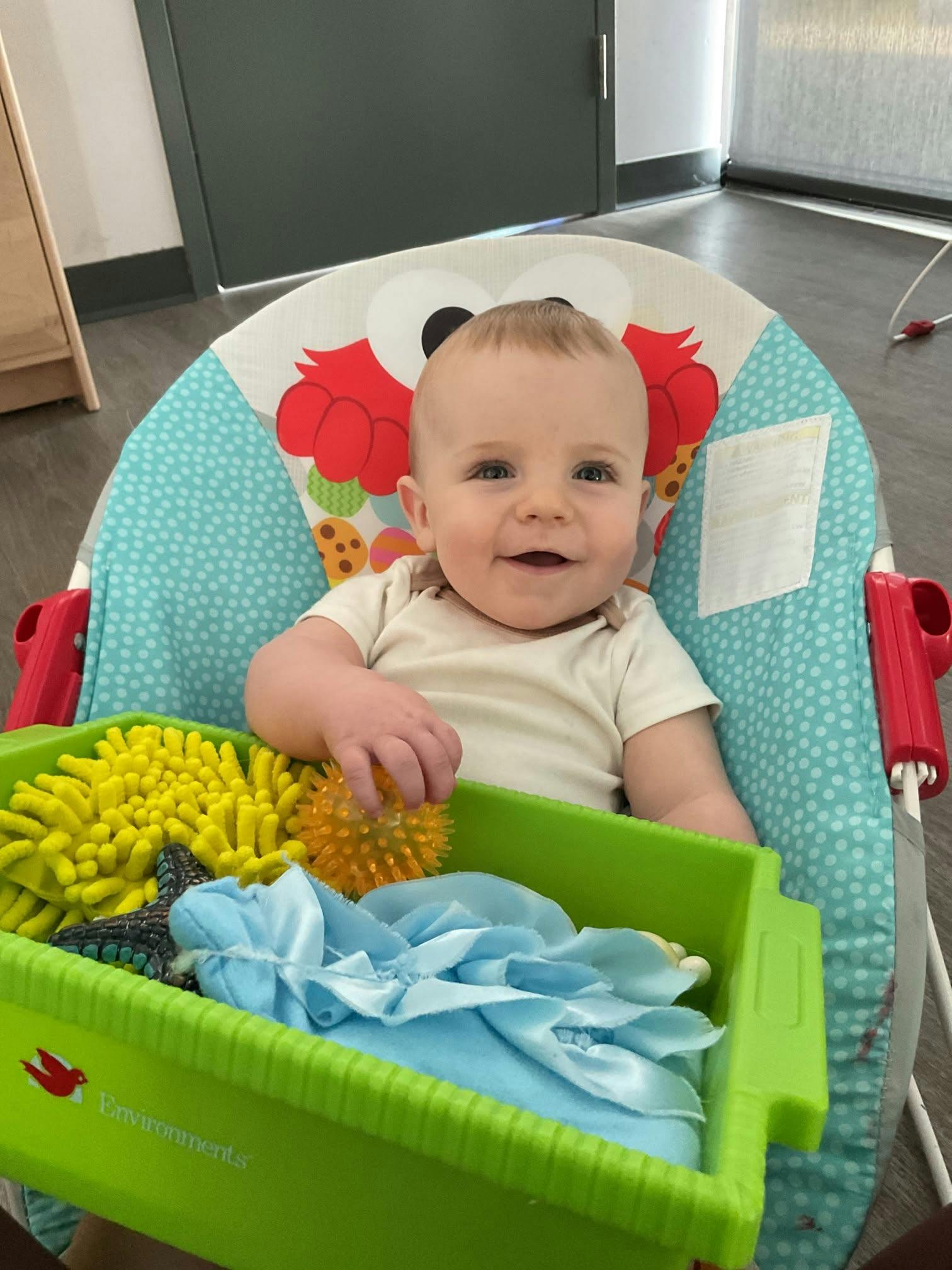 A baby sitting in a bouncer seat holding a toy