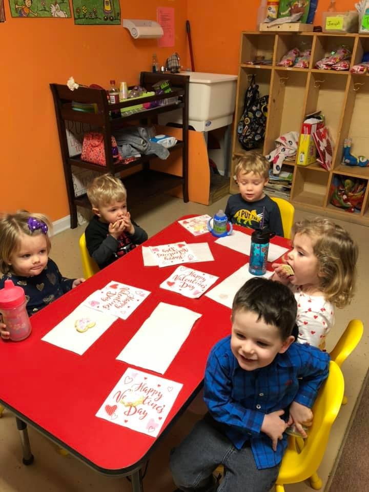 Four children and one teen sitting at a red table with cards