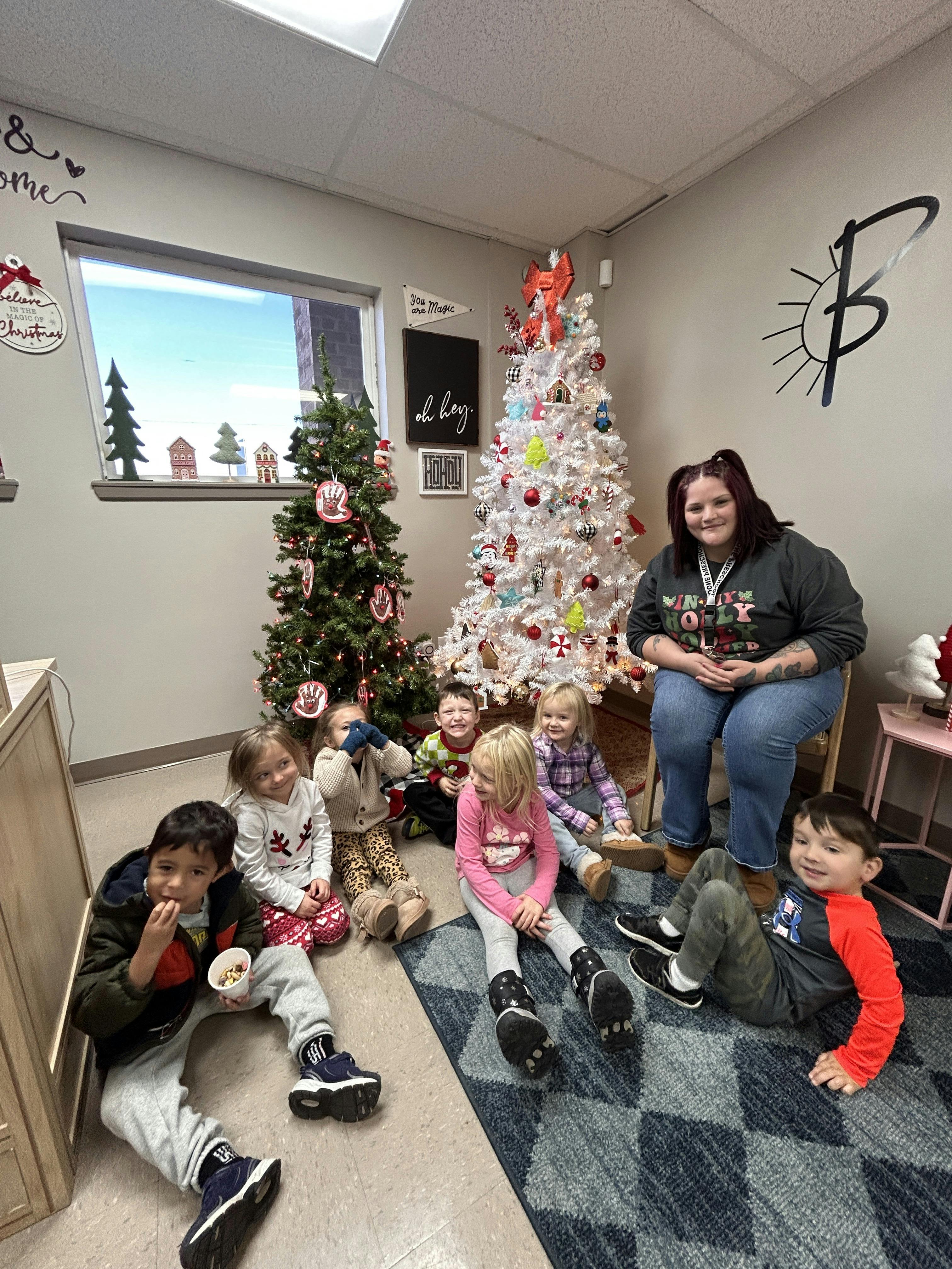 Adult and six children sitting on the floor with Christmas trees