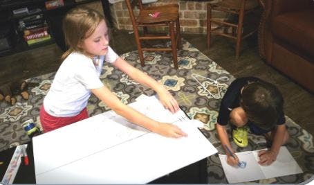 Two children drawing on paper on a patterned rug