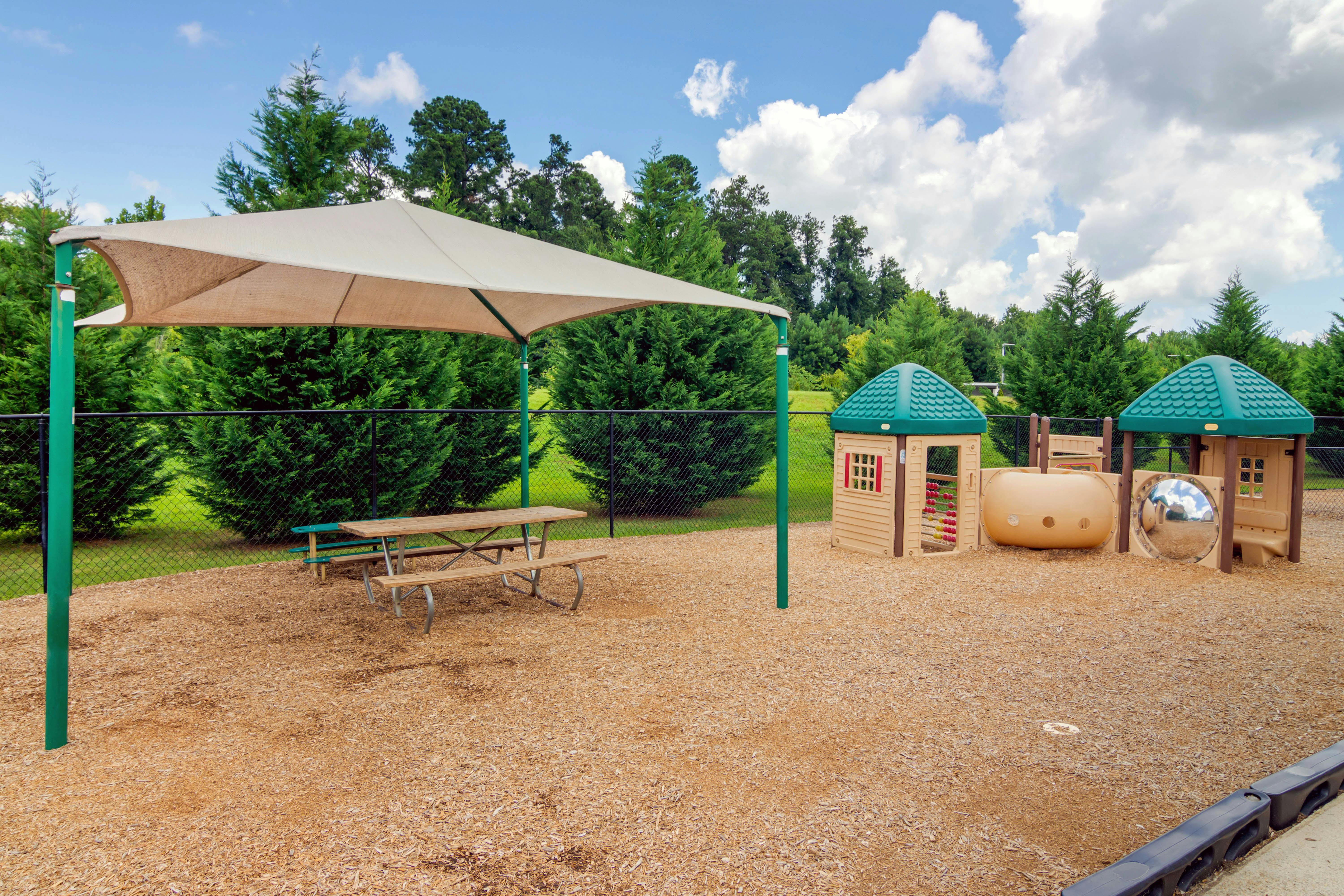 Playground area with wood chips, shade structure, picnic table, and playhouses