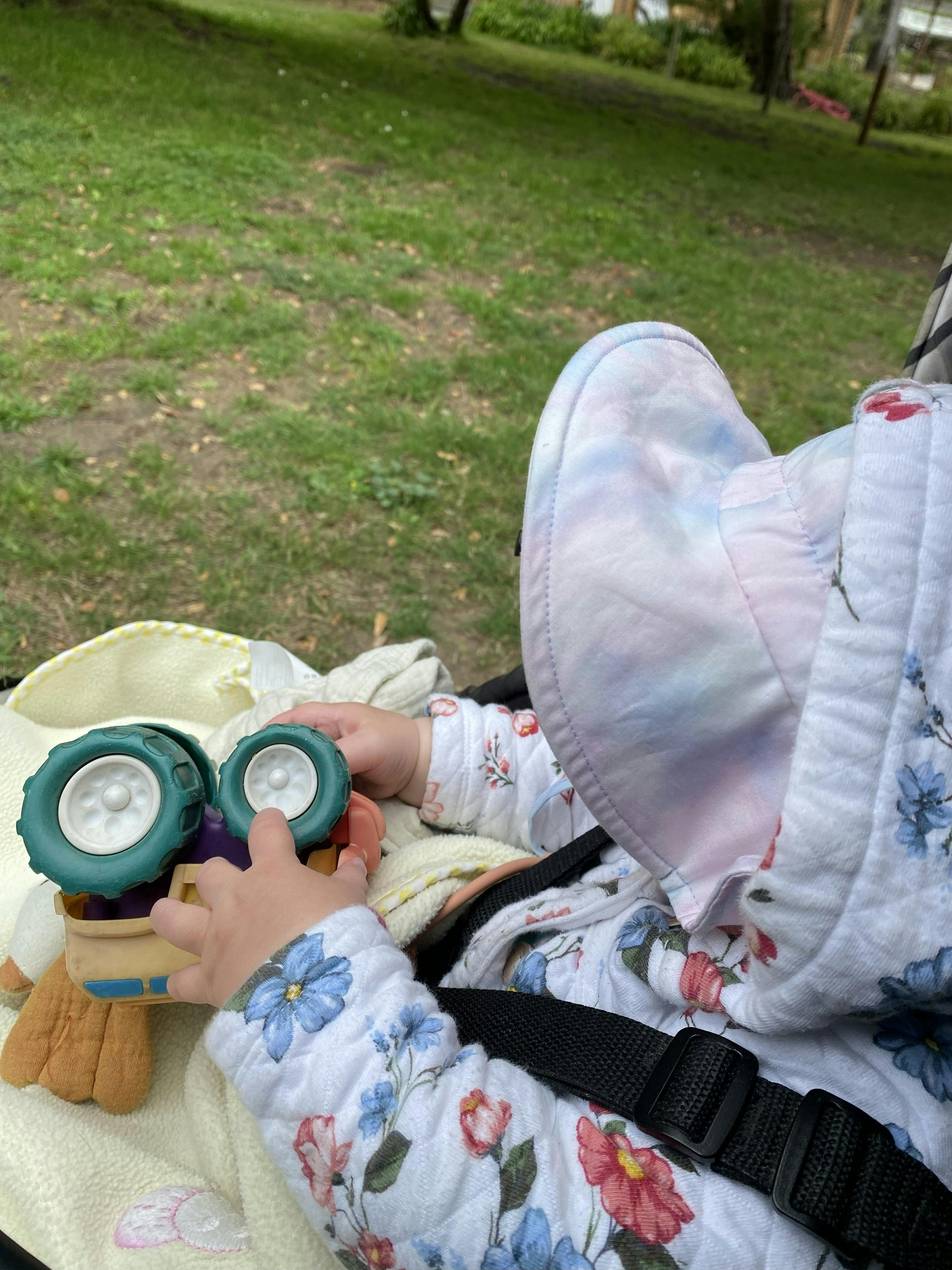 Child in a floral outfit and tie-dye hat playing with a toy truck