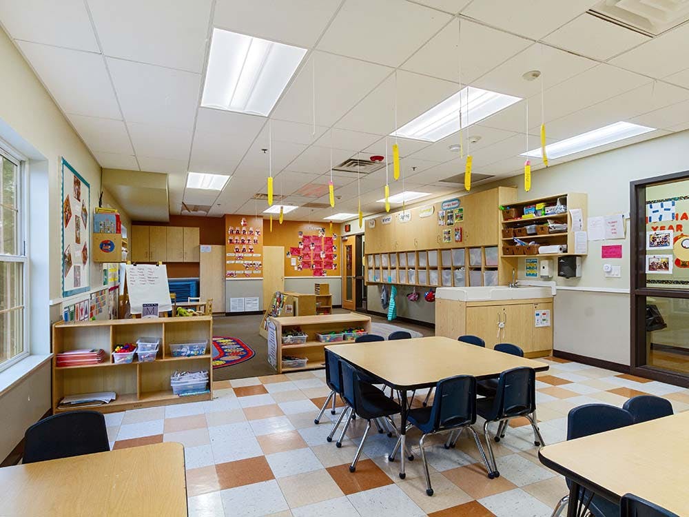 Empty classroom with small tables and chairs, cubbies, and bulletin boards