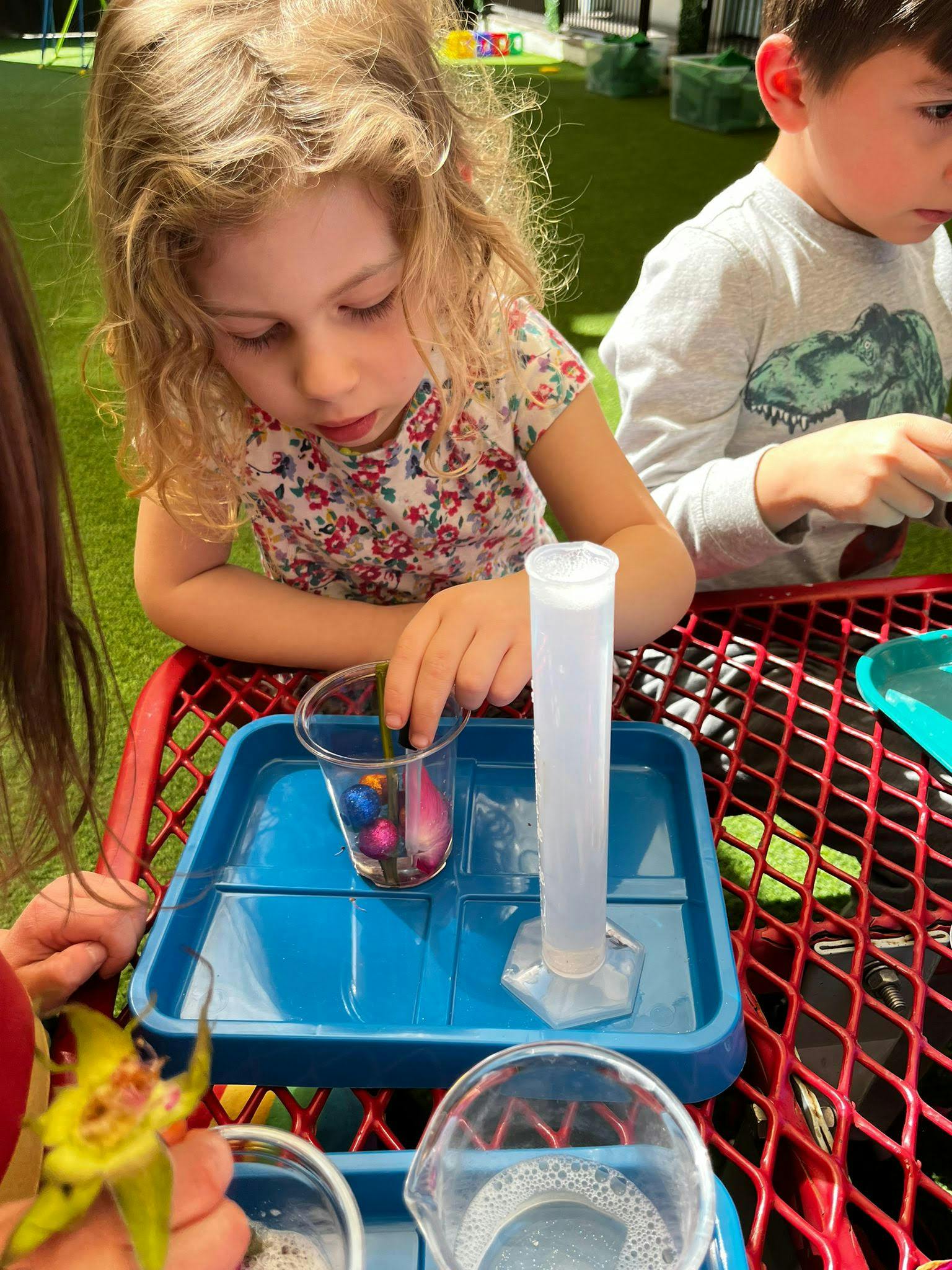 Child playing with colorful objects in a cup and a measuring cylinder