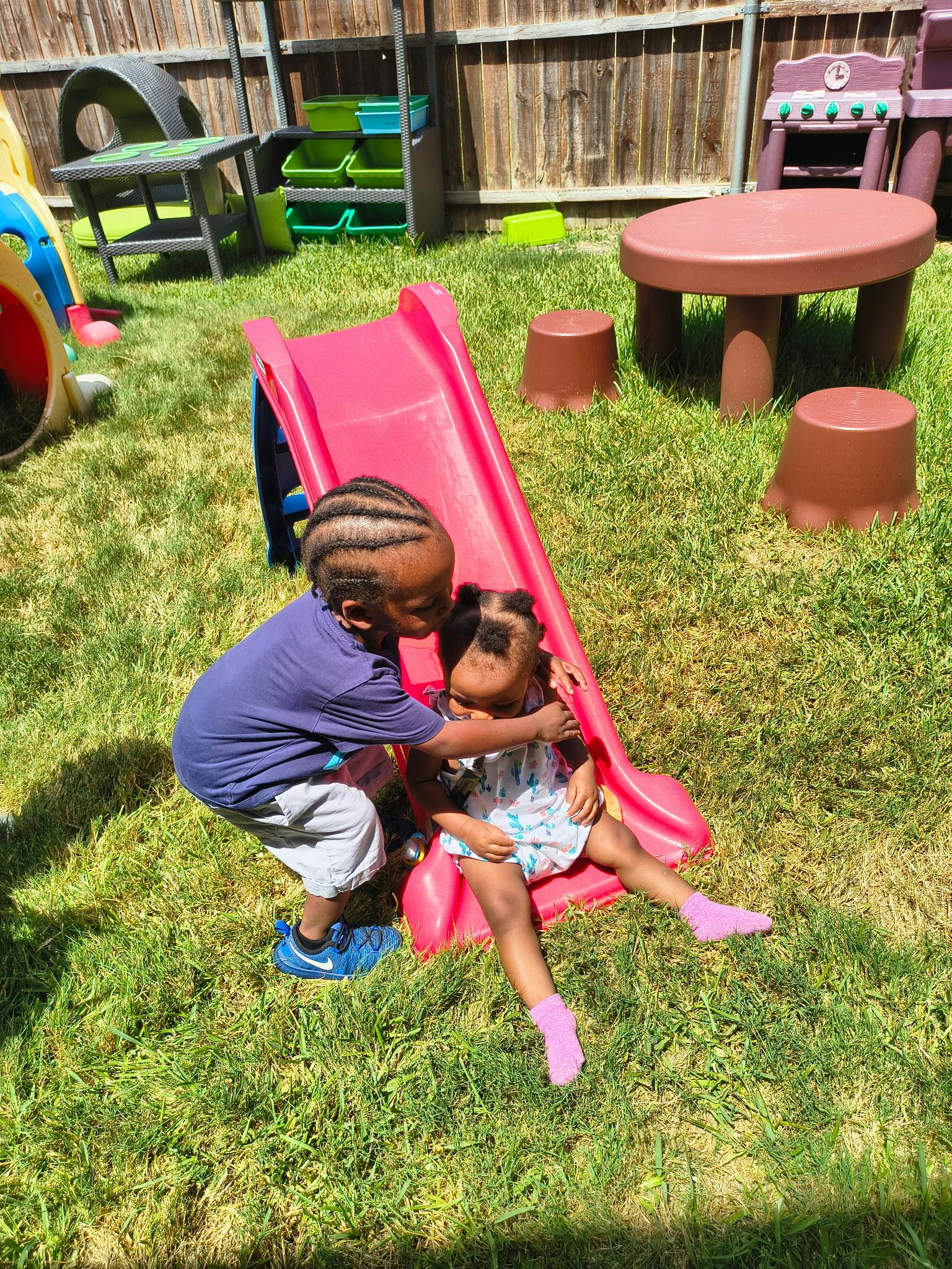 Child leaning over to hug another child sitting on a small plastic slide
