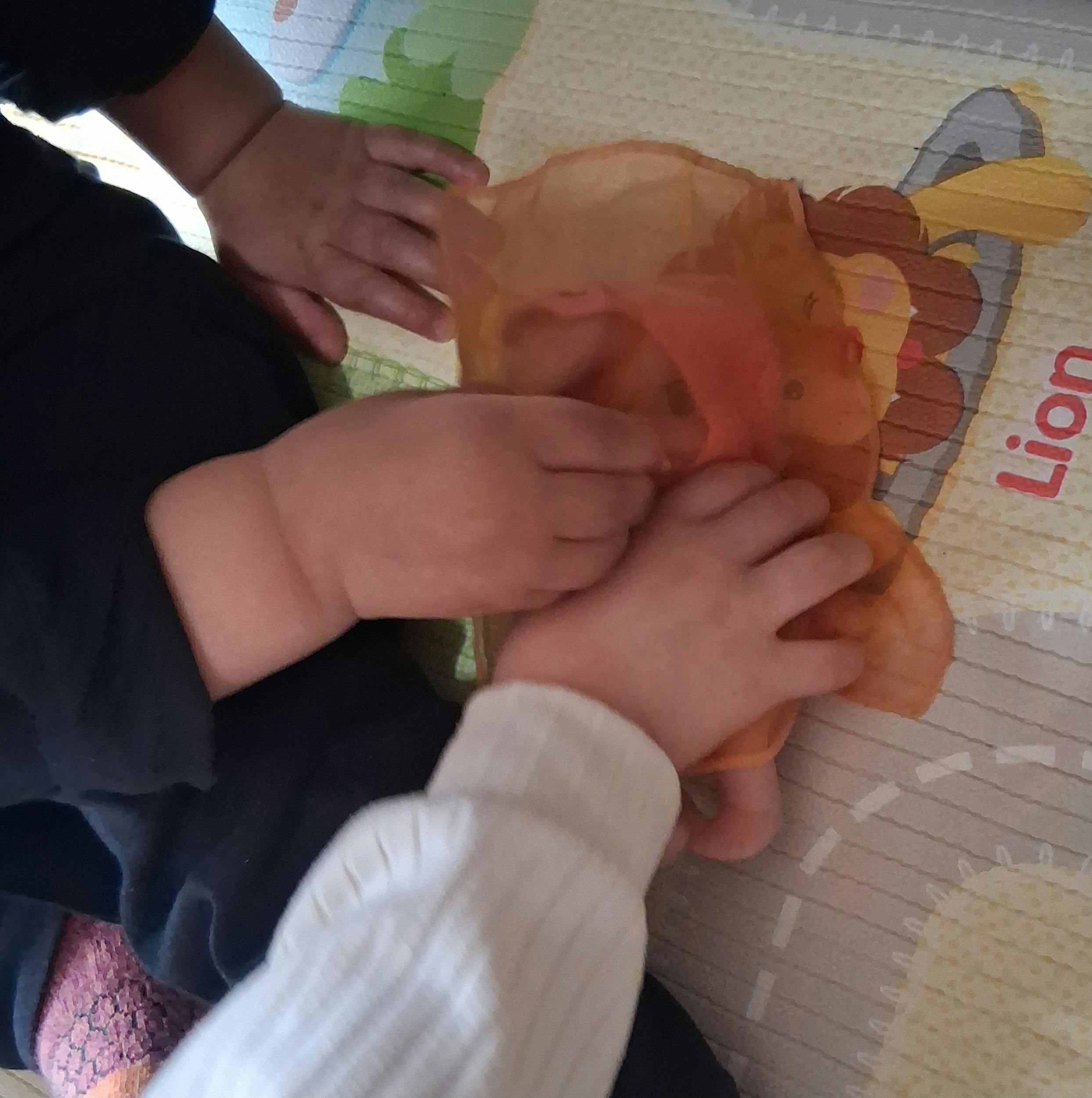 Child's hands playing with orange fabric on a playmat