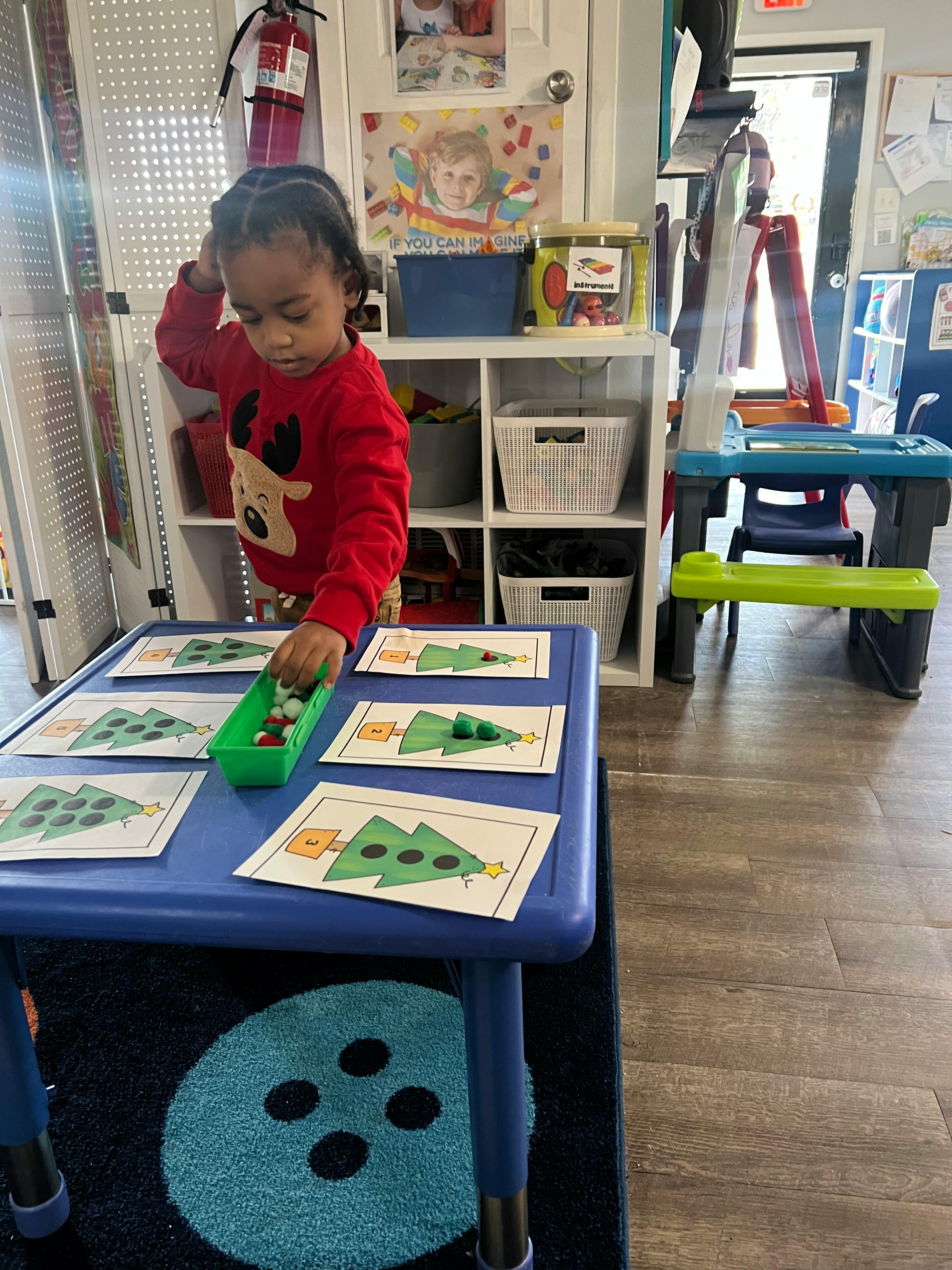 Child placing small objects on a card with a Christmas tree design