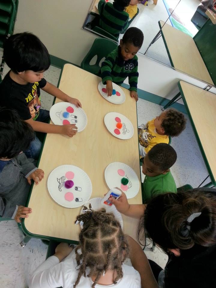 Children at a table doing crafts with paper plates and pom-poms