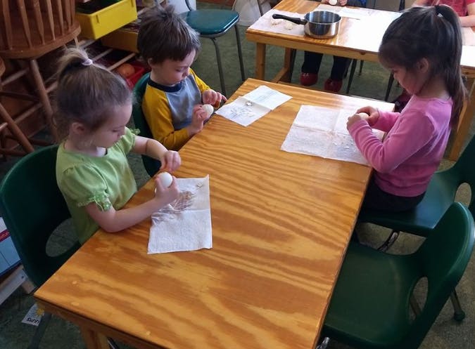 Three children at a table with paper and eggs