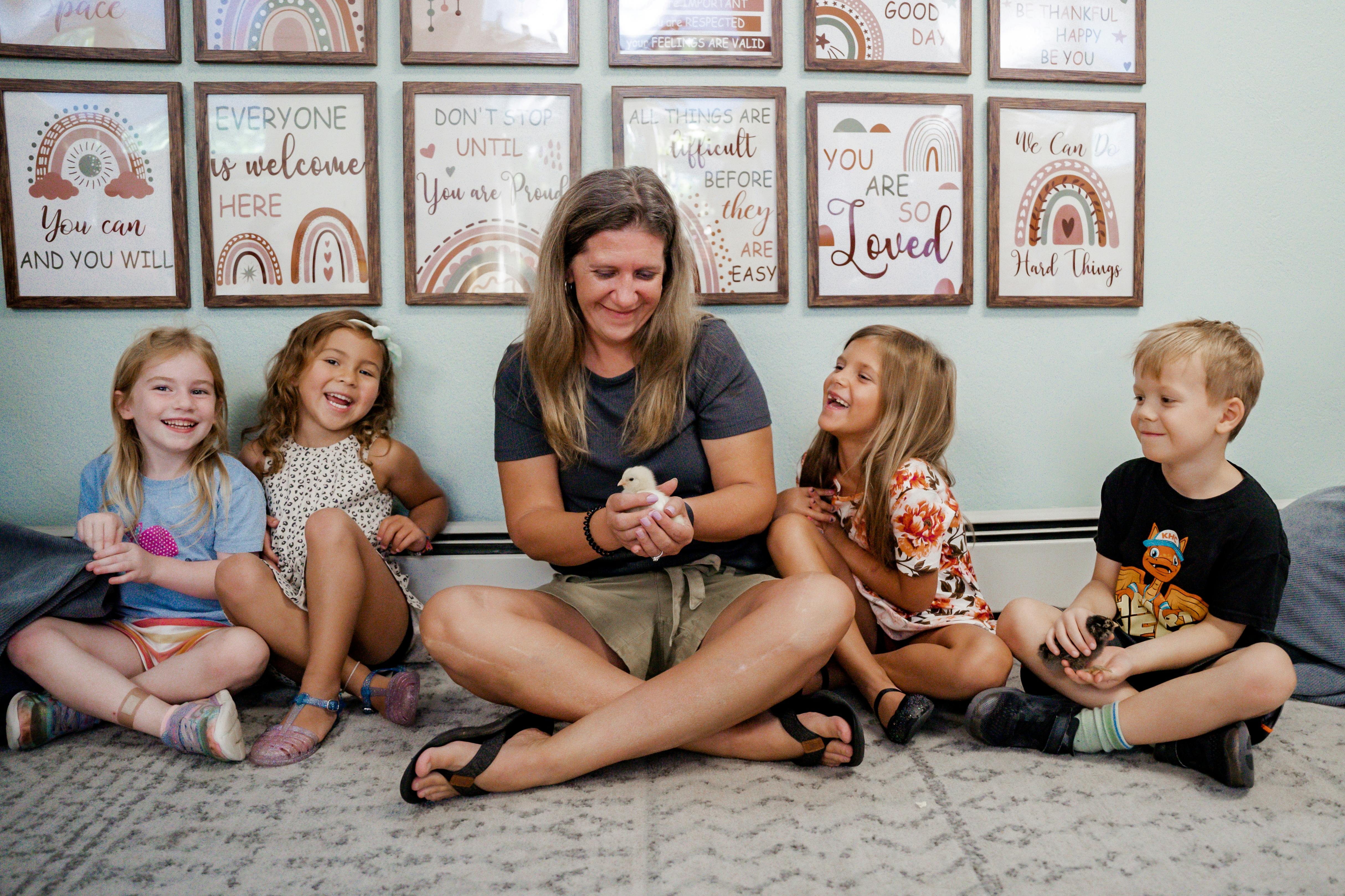 Adult and three children sitting on floor, adult holding a chick