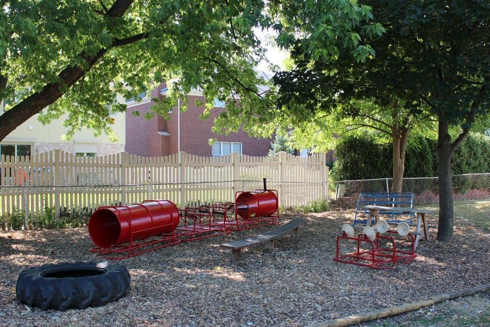 Playground with red barrels, a tire, and a wooden fence