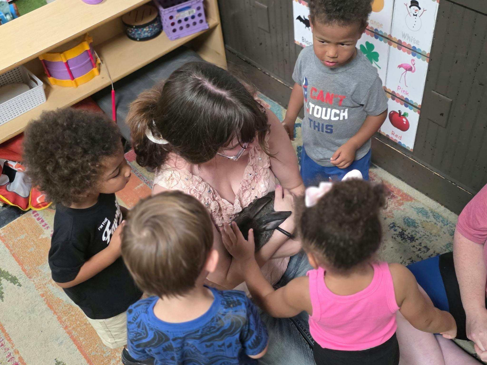 A person holding a rabbit while surrounded by children in a classroom
